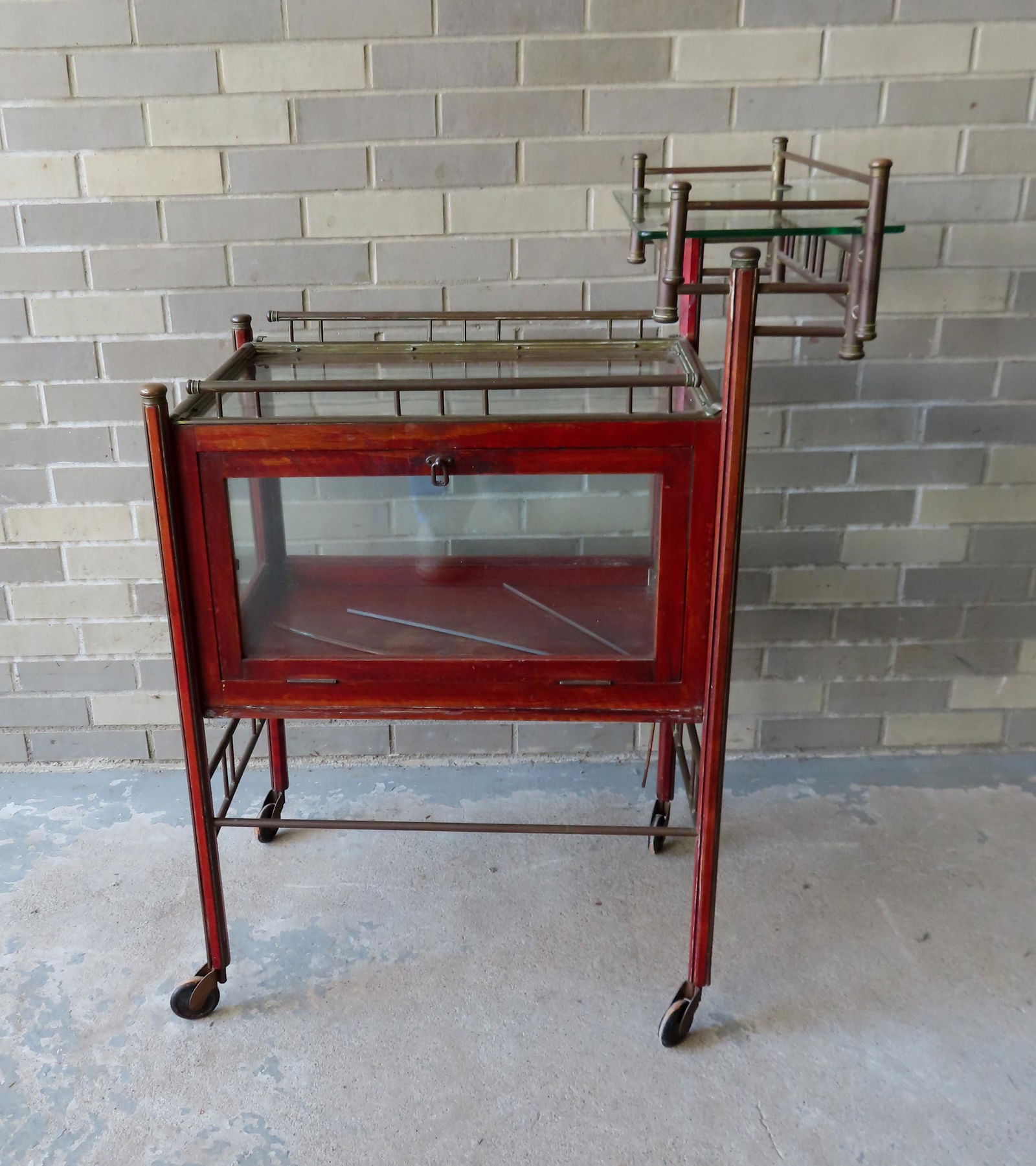 An unusual tea cart with a wooden frame housing a: An unusual tea cart with a wooden frame housing a showcase below with lift-top door - the top also with a step-back brass gallery with glass shelf. Early 20th century. Some surface wear to finish on w