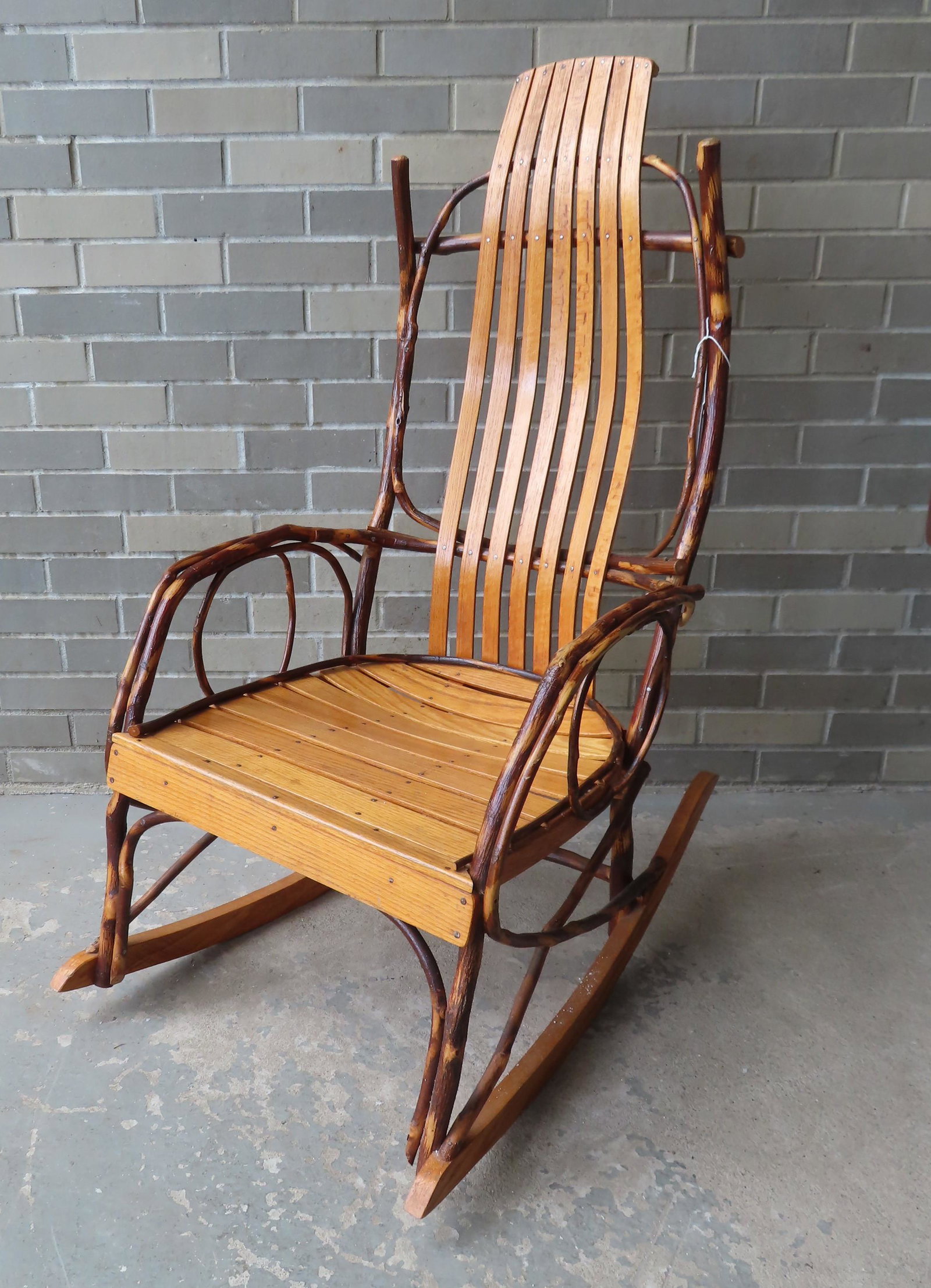 A rustic Amish twig rocker. The back and seat with: A rustic Amish twig rocker. The back and seat with shaped oak slats, 3rd quarter 20th century. Very good condition. 55"H x 22"W x 33 3/4"D.