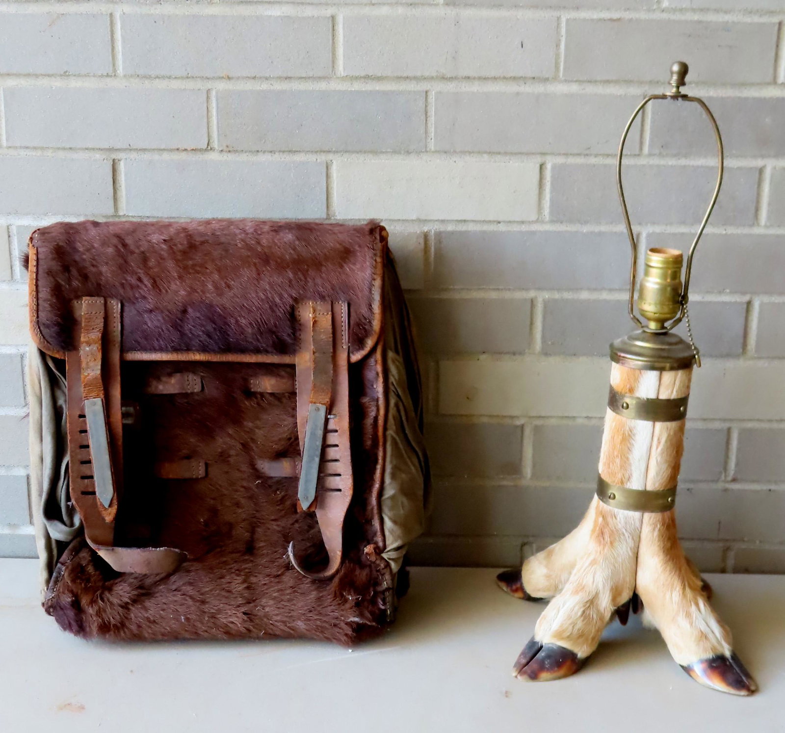 Two rustic collectibles including: A deer foot table: Two rustic collectibles including: A deer foot table lamp - 21"H - good condition; and a backpack that appears to be constructed from a bear hide - a buckle is broken, otherwise with original straps a