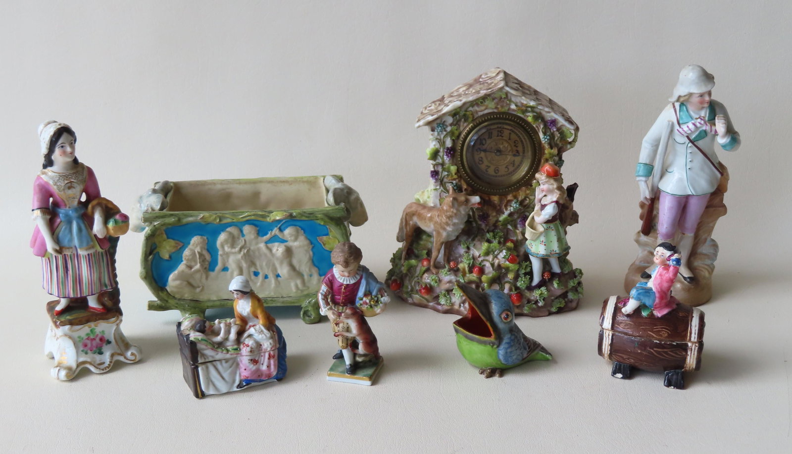 A grouping of 7 mostly English and German figures.: A grouping of 8 mostly English and German hand painted figural porcelain collectibles including: A Little Red Riding Hood porcelain clock arrangement with cottage, wolf, girl with red hat, all standin