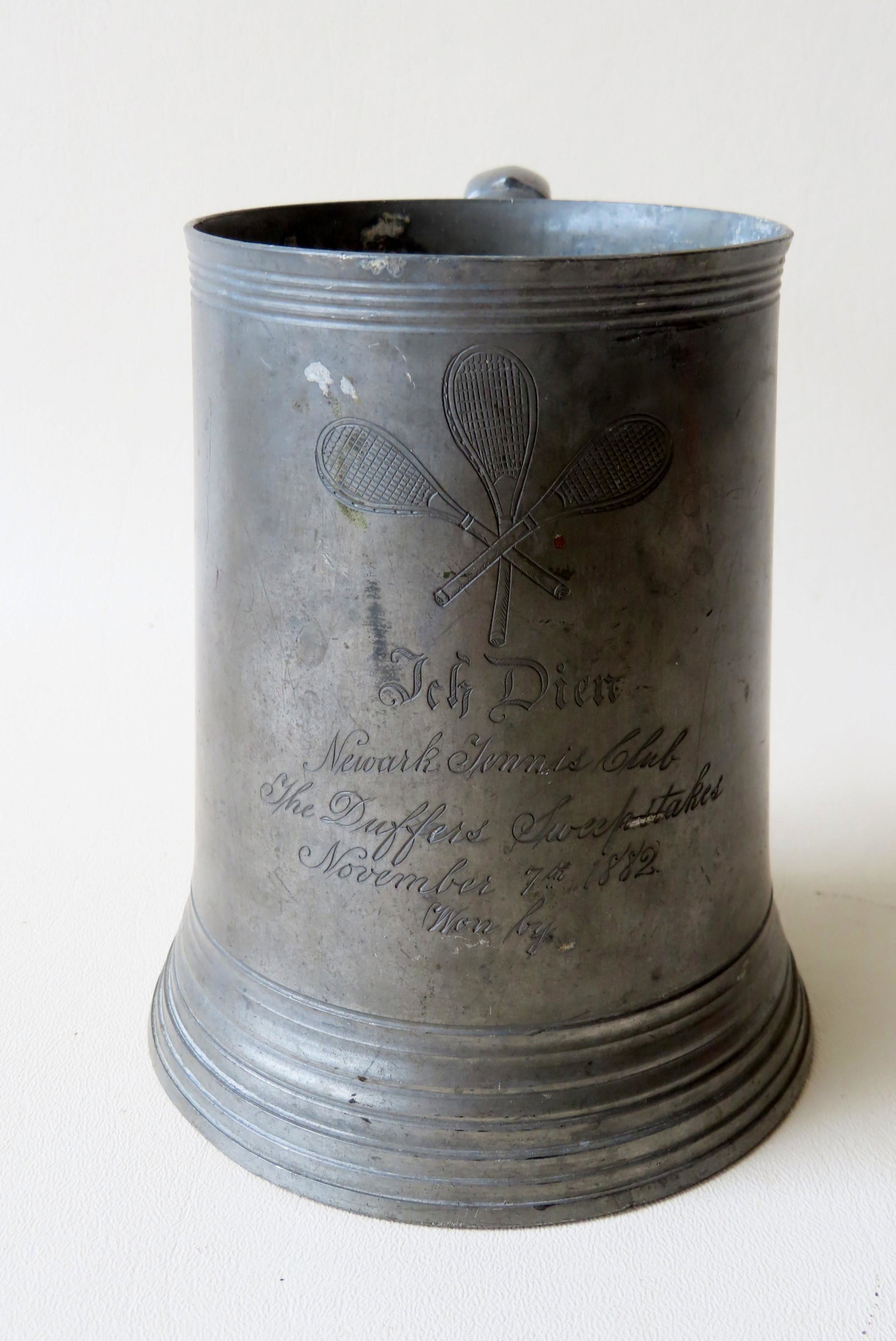 Early American pewter tennis trophy mug with glass: Early American pewter tennis trophy mug with glass bottom - the front engraved "Ich Dien (I Serve) / Newark Tennis Club / The Duffers Sweepstakes / Nov. 7th 1882 / Won by ". Scrolled handle and steppe