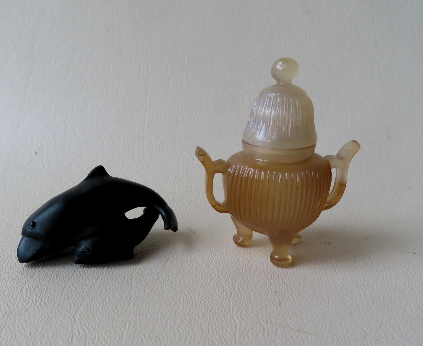Two miniature oriental decorative objects: 1) A carved: Two miniature oriental decorative objects: 1) A carved netsuke in the form of a dolphin with calf, appears to be ebony wood - measures 2 1/8"L - unknown age; together with a miniature jade teapot 2 1/