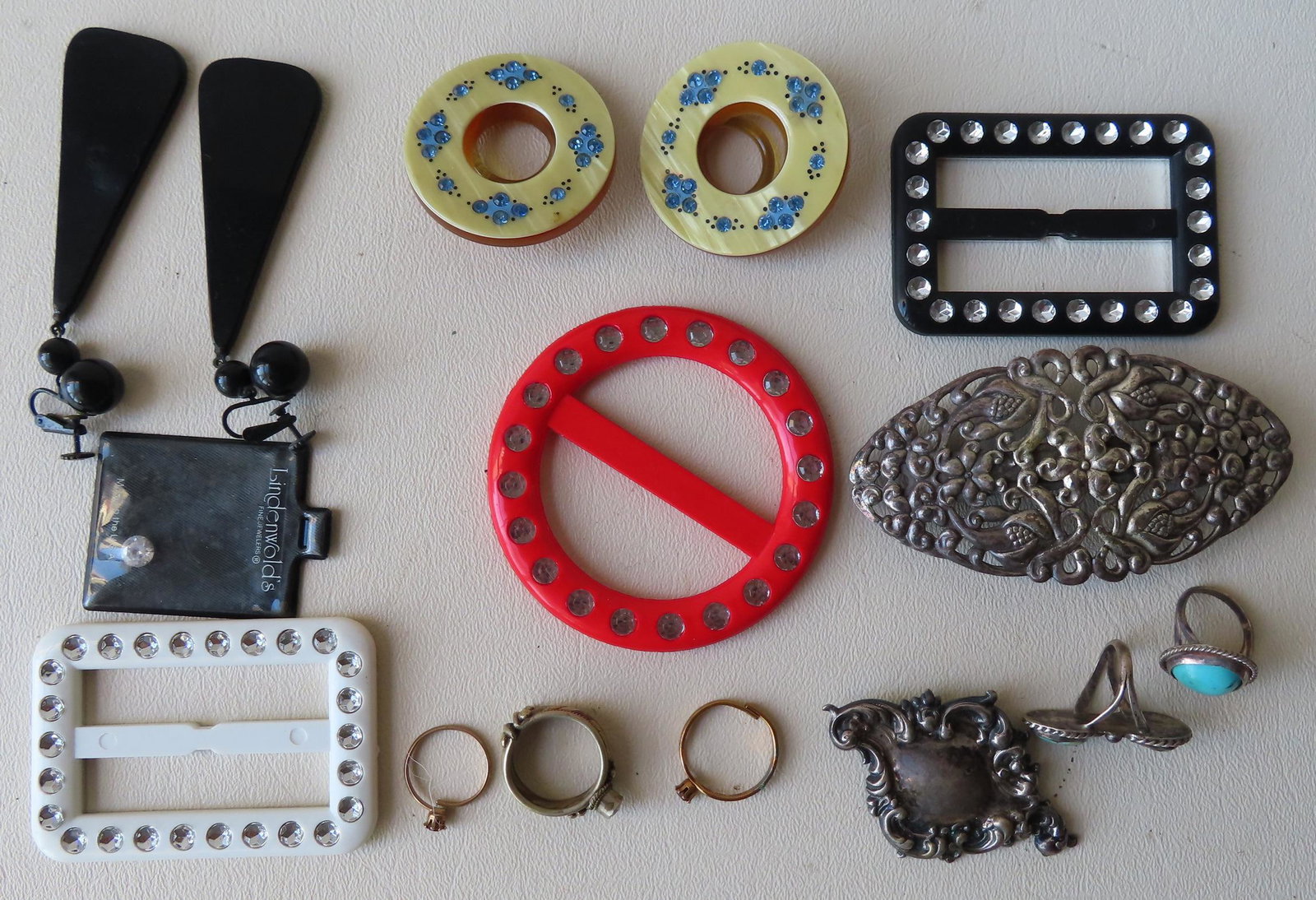 Grouping of miscellaneous jewelry including: Two: Grouping of miscellaneous jewelry including: Two unmarked silver broaches, 3 colorful plastic buckles with rhinestones, 2 circular Bakelite ornaments with applied rhinestones within hand painted flowe