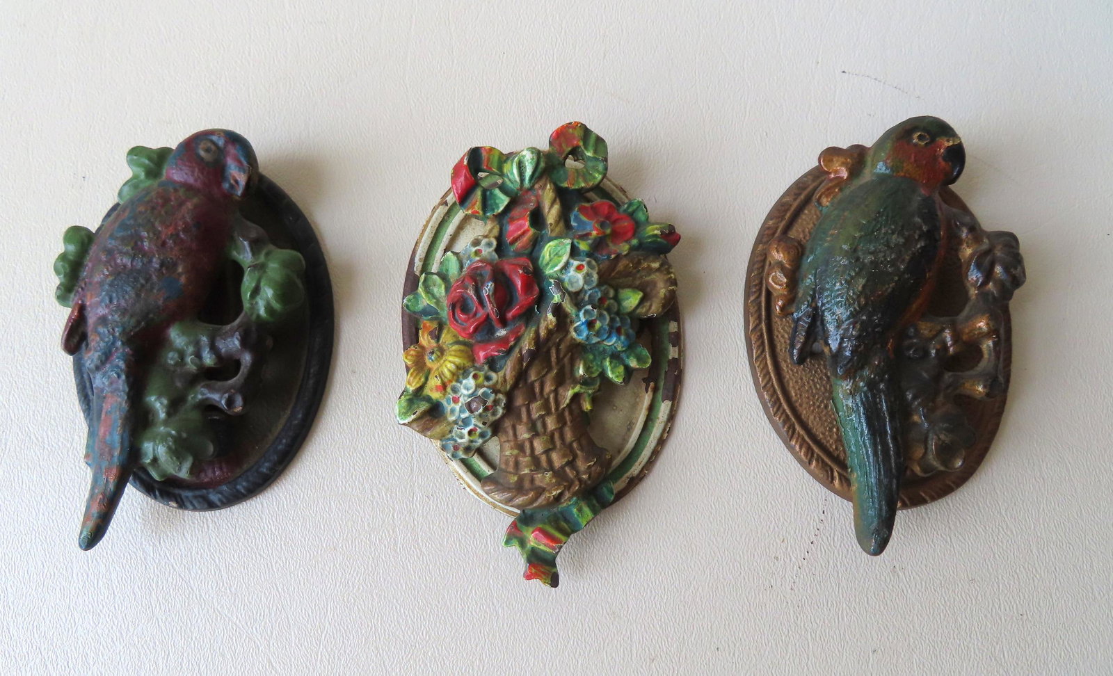 Grouping of 3 cast iron door knockers in original: Grouping of 3 cast iron door knockers in original paint, early 20th century. Includes 2 parrots and 1 basket of flowers. All in very good condition. The largest 4 5/8"H x 2 7/8"W.