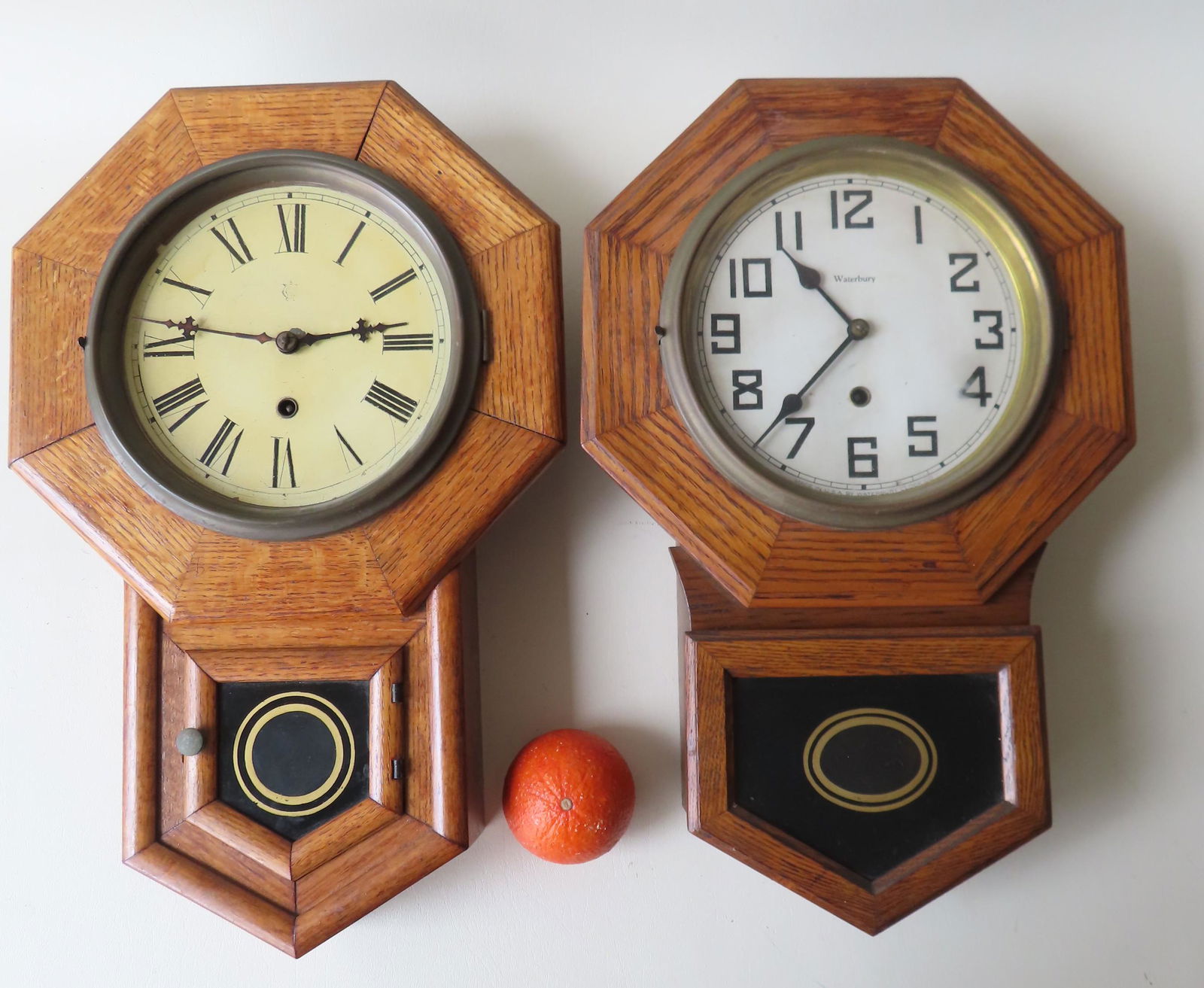 Two oak regular wall clocks including: Waterbury Clock: Two oak regular wall clocks including: Waterbury Clock Co. - with key and pendulum; unknown maker, complete with key and pendulum - lower door is off hinges and needs repair. Both clocks appear in goo