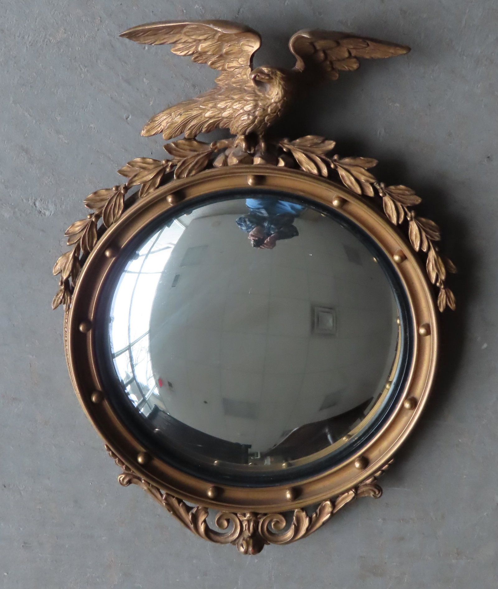 A petite bull's-eye mirror with carved gilt gesso: A petite bull's-eye mirror with carved gilt gesso spread wing eagle finial, probably late 19th to early 20th century. Very good original condition. Measures 14 1/4"W x 20"H x 2 13/4"depth.
