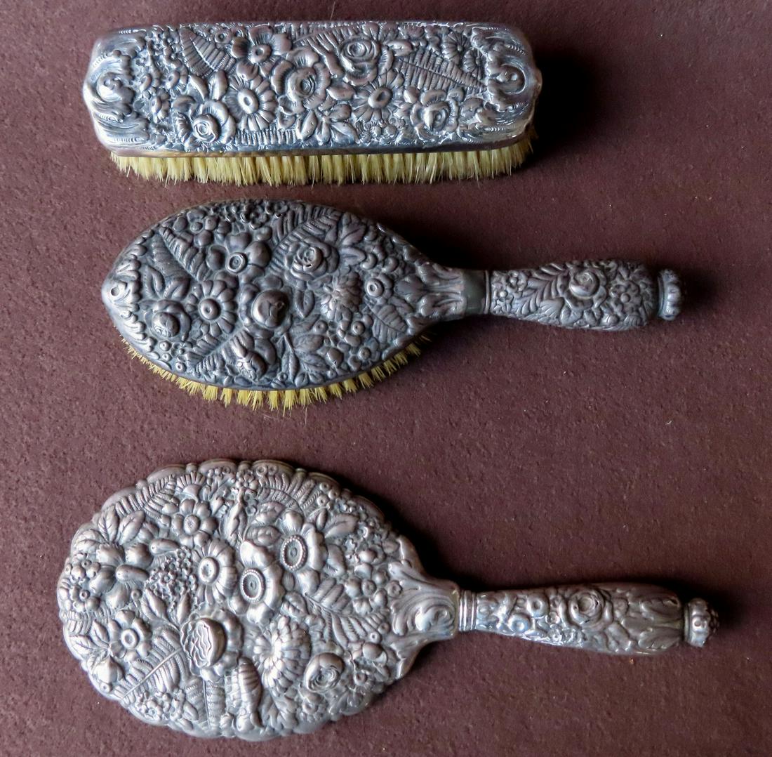 A Tiffany and Co. 3 piece repousse dresser set: A Tiffany and Co. 3 piece repousse dresser set consisting of hand mirror, and 2 brushes - the handled brush has been repaired at neck and partially obscures the Tiffany signature - the other brush is 