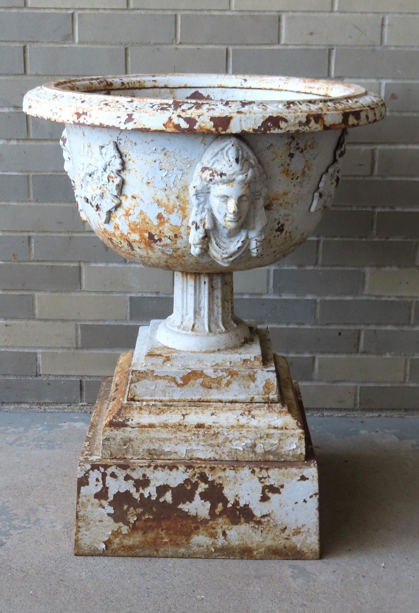 A cast iron garden urn mounted on a double stepped base, having a basin decorated with 3 applied (1 of 4)
