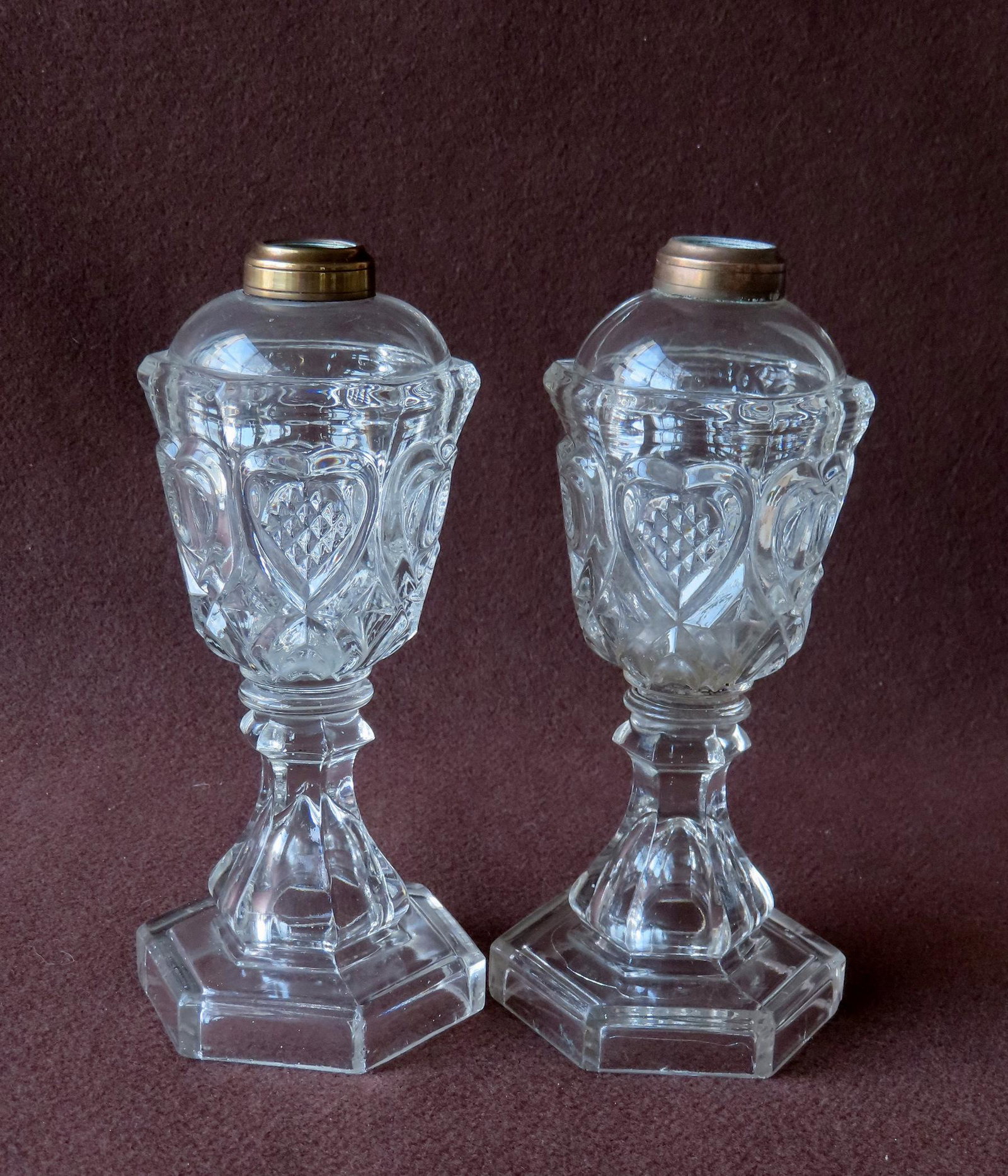 Two matching pattern glass whale oil lamps having an oil font decorated with embossed hearts, mid: Two matching pattern glass whale oil lamps having an oil font decorated with embossed hearts, mid 19th century or earlier. Each having the typical glass wafer attaching the oil font to the base. Both 