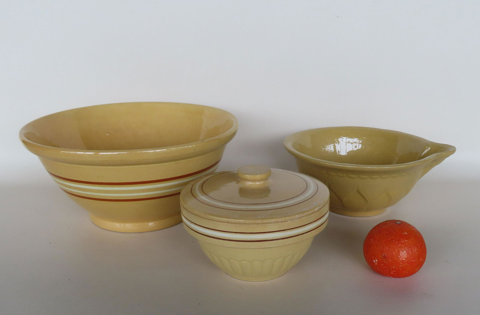Three yellowware bowls. The largest a mixing bowl on footed base and having brown and white bands: Three yellowware bowls. The largest a mixing bowl on footed base and having brown and white bands and rolled rim - 13" diameter x 6"H; a batter bowl on footed base with embossed designs on sides - 10