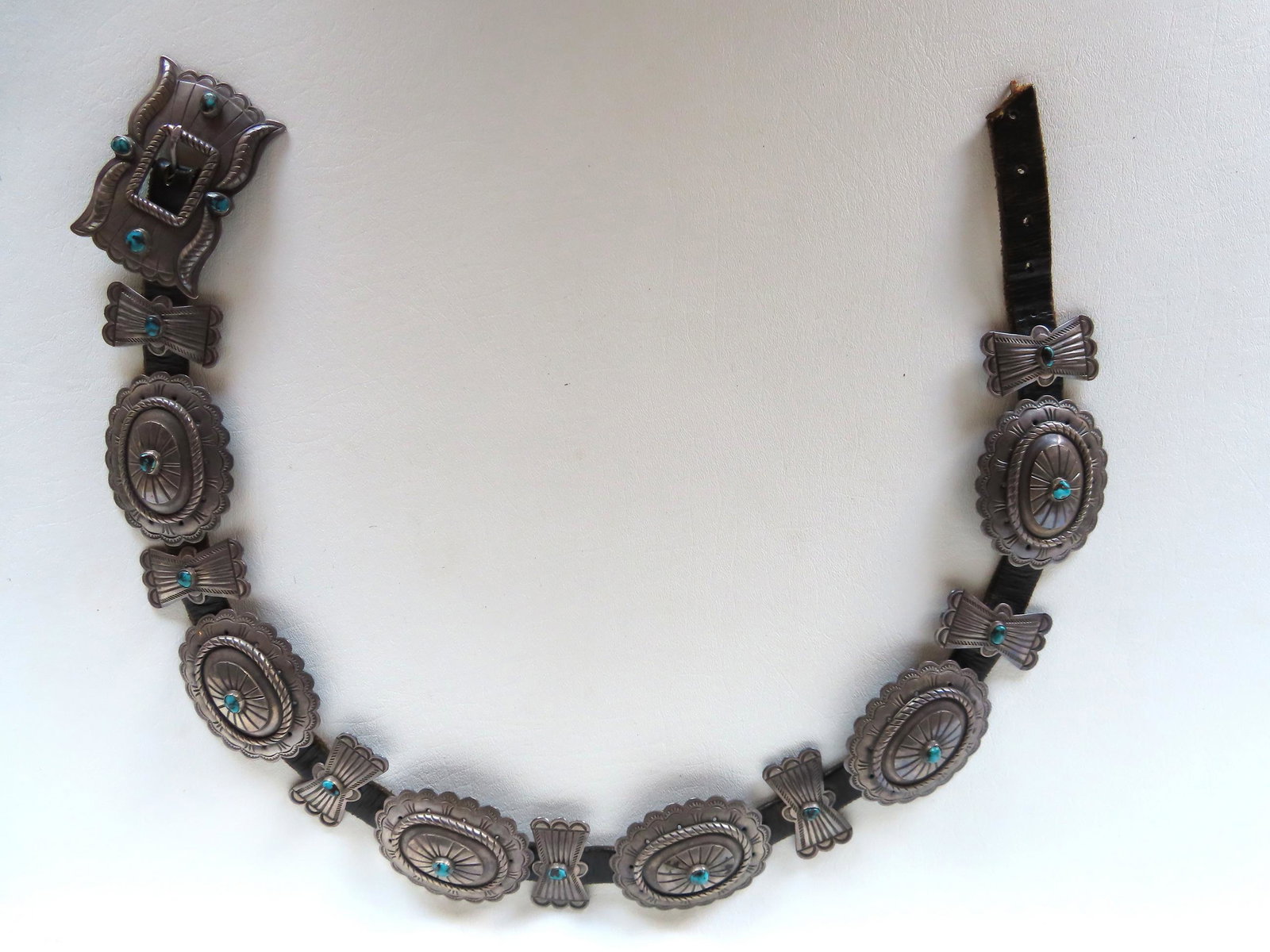 A Navajo Concho belt decorated with 13 butterfly and oval shaped sterling silver conchos each: A Navajo Concho belt decorated with 13 butterfly and oval shaped sterling silver conchos each having a center with a small applied turquoise ornament and the silver buckle decorated with 4 turquoise s