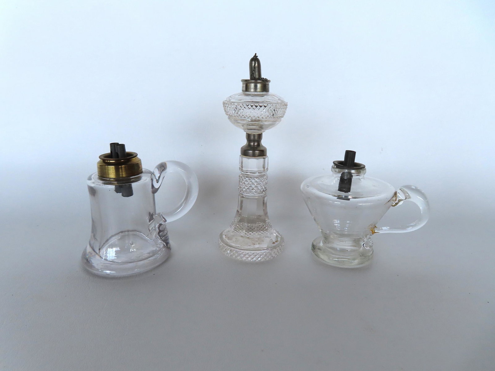 Three fluid lamps including: 1) An unusual cut glass fluid burning lamp, late 19th century - very: Three fluid lamps including: 1) An unusual cut glass fluid burning lamp, late 19th century - very good condition - measures 5 3/4"H; 2) A whale oil spark lamp with finger holder - possibly with small 