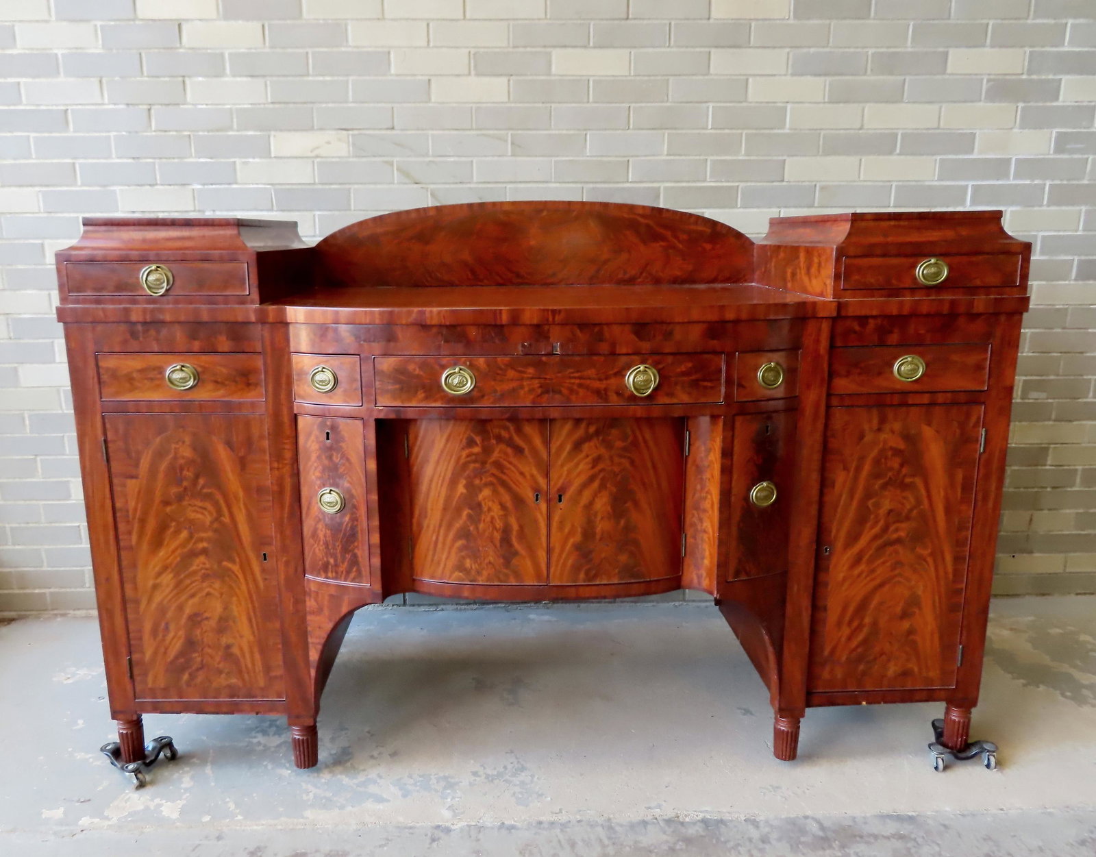 A very fine late Sheraton mahogany sideboard having a bow front with multiple drawers over 2 doors: A very fine late Sheraton mahogany sideboard having a bow front with multiple drawers over 2 doors flanked by fitted liquor drawers. The bow front is flanked by 2 drawers over door - arched backsplash