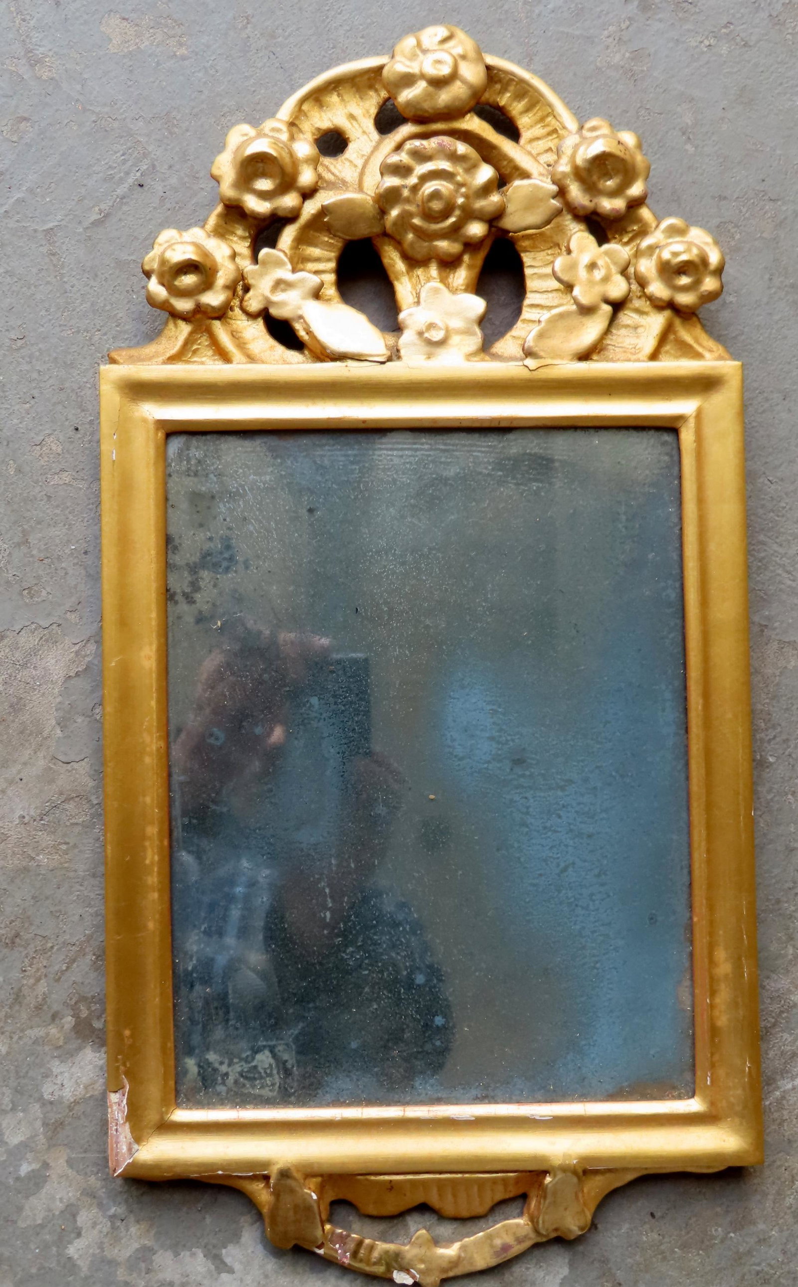 A small gilt gesso 18th century continental mirror having a crest decorated with flowers. The: A small gilt gesso 18th century continental mirror having a crest decorated with flowers. The gilding is old, but likely not original. Minor gesso losses, and the silvering of original mirror has dete