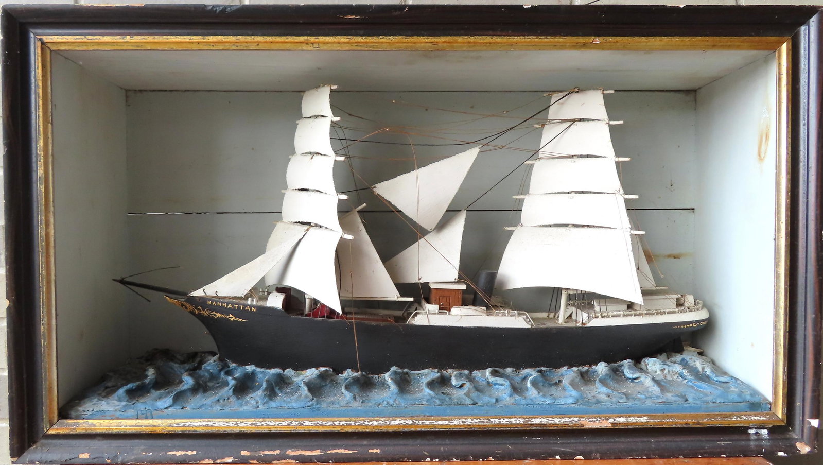 A sailing ship diorama depicting a hand made wooden rigged 2 mast sailing vessel named "Manhattan": A sailing ship diorama depicting a hand made wooden rigged 2 mast sailing vessel named "Manhattan" in carved wavy waters - all in original paint, 19th century. Some of the lines have broken and need t