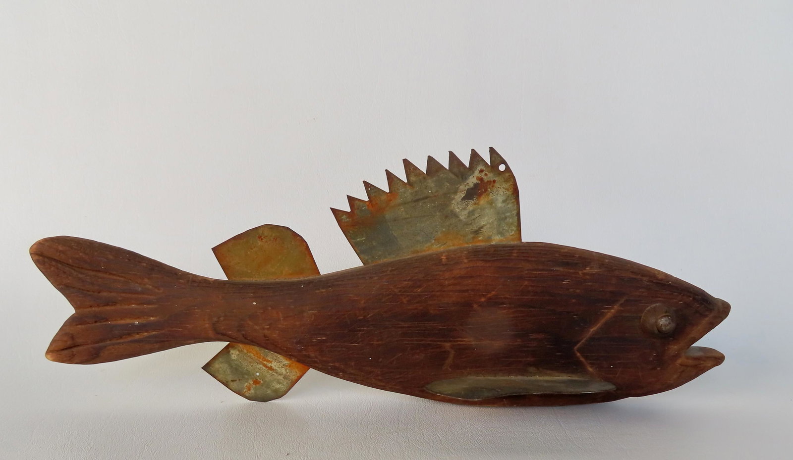 A large and heavy hand carved ice fishing decoy in original unpainted patinated surface with sheet: A large and heavy hand carved ice fishing decoy in original unpainted patinated surface with sheet tin fins, carved open mouth with shaped lips, carved gills, and bulging tack eyes - circa 1930-40 - m