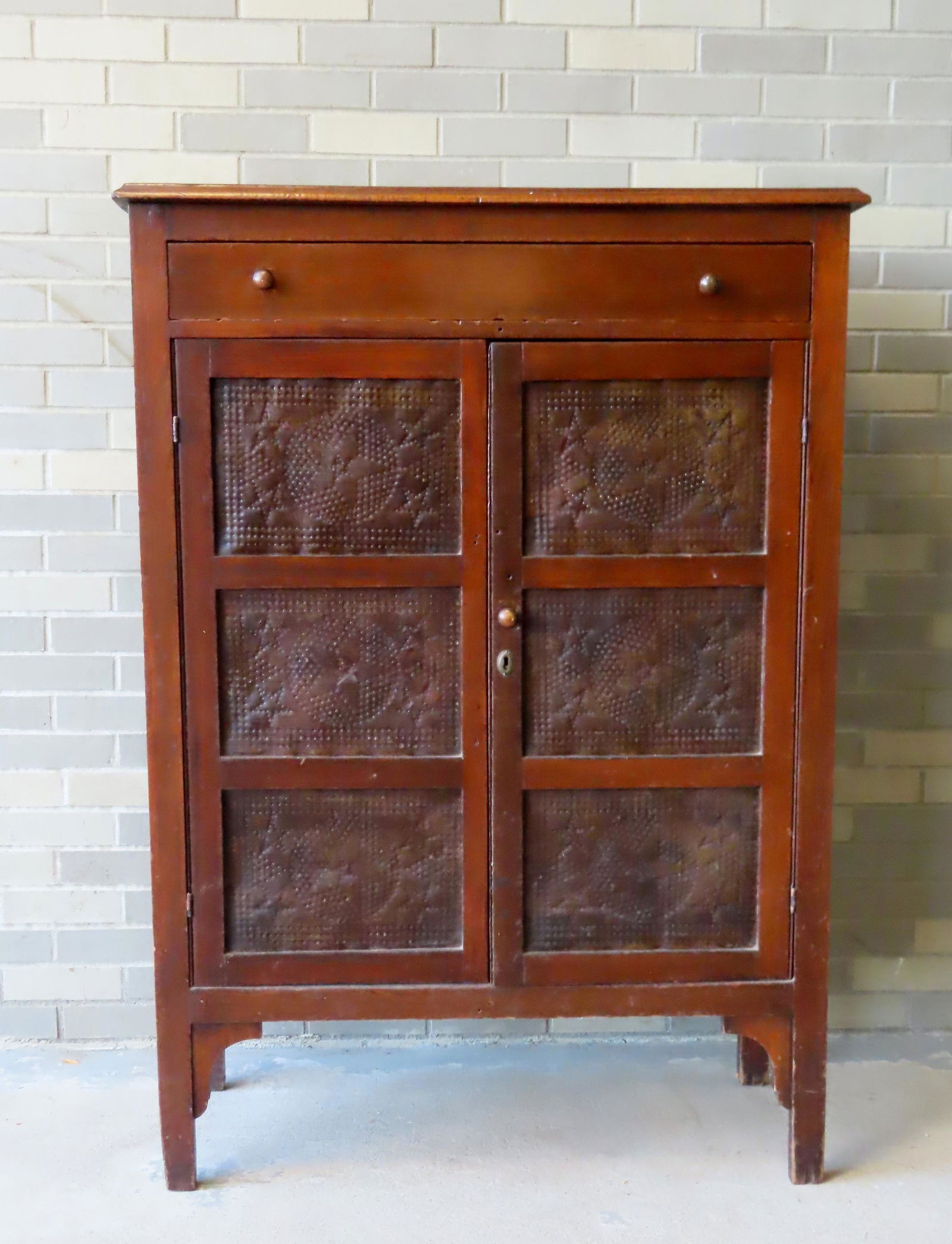 A pierced tin pie safe having a single long dovetailed drawer over 2 doors, each decorated with 3: A pierced tin pie safe having a single long dovetailed drawer over 2 doors, each decorated with 3 pierced tin panels of stars. The sides also with 3 pierced tin panels of stars. Old red stain - circa