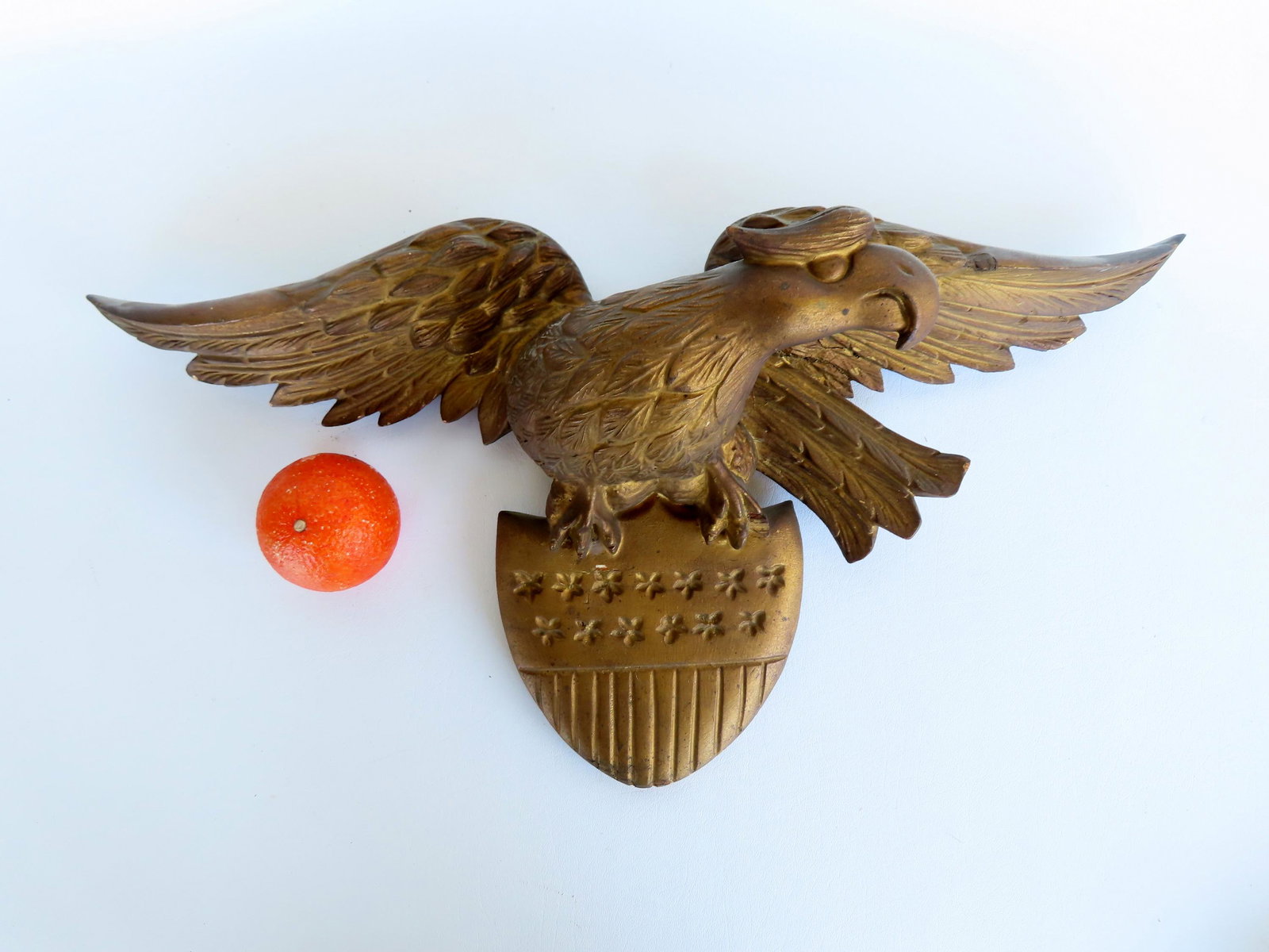 A spread wing eagle wall plaque mounted on an American shield in original gilt, late 19th century,: A spread wing eagle wall plaque mounted on an American shield in original gilt, late 19th century, very good condition. Measures 24"W x 6 1/2"D x 11"H.