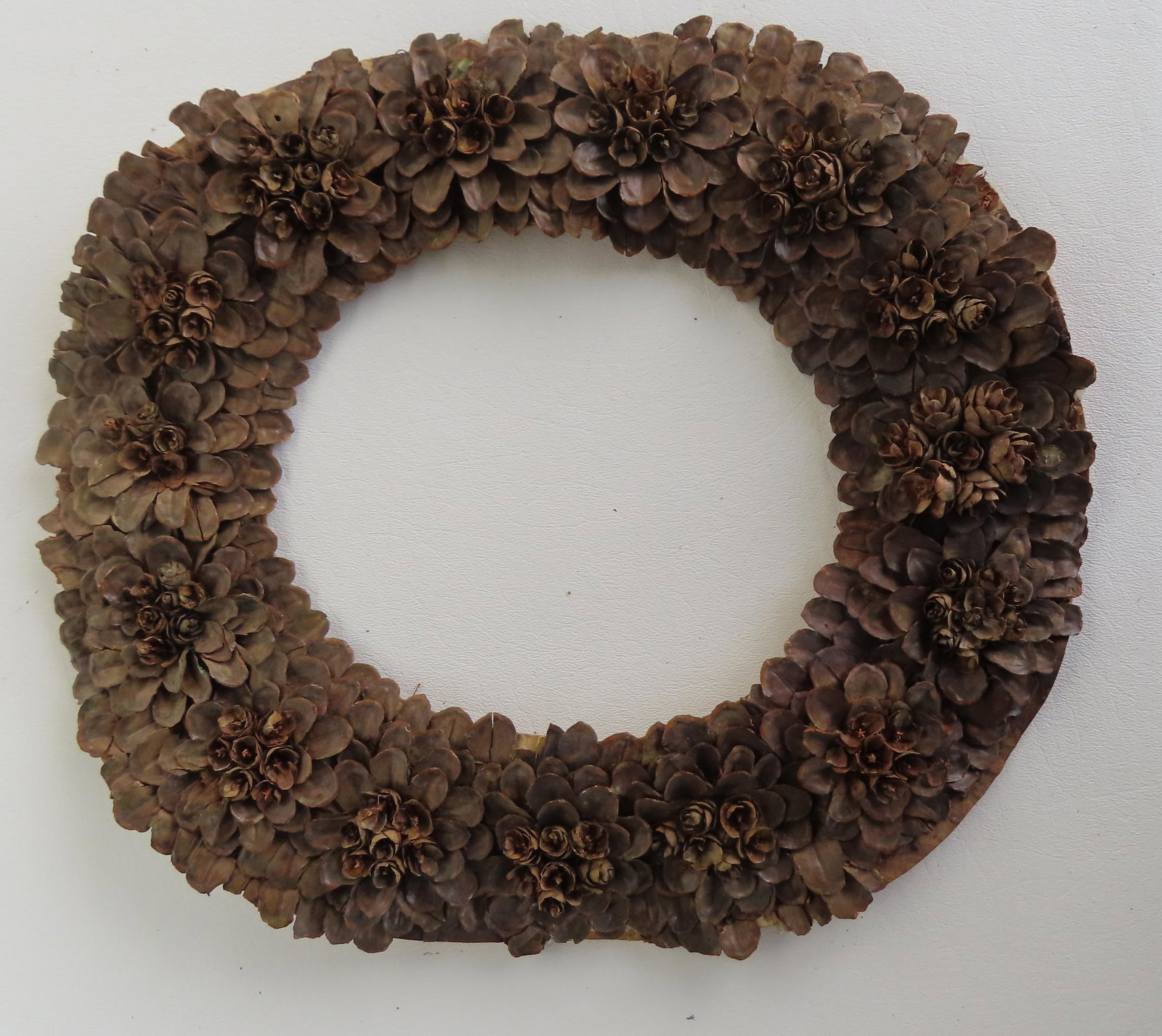 A hand made wreath constructed from pine cones hand sewn to a leather backing, 19th century.: A hand made wreath constructed from pine cones hand sewn to a leather backing, 19th century. Measures 11 1/2" x 13".