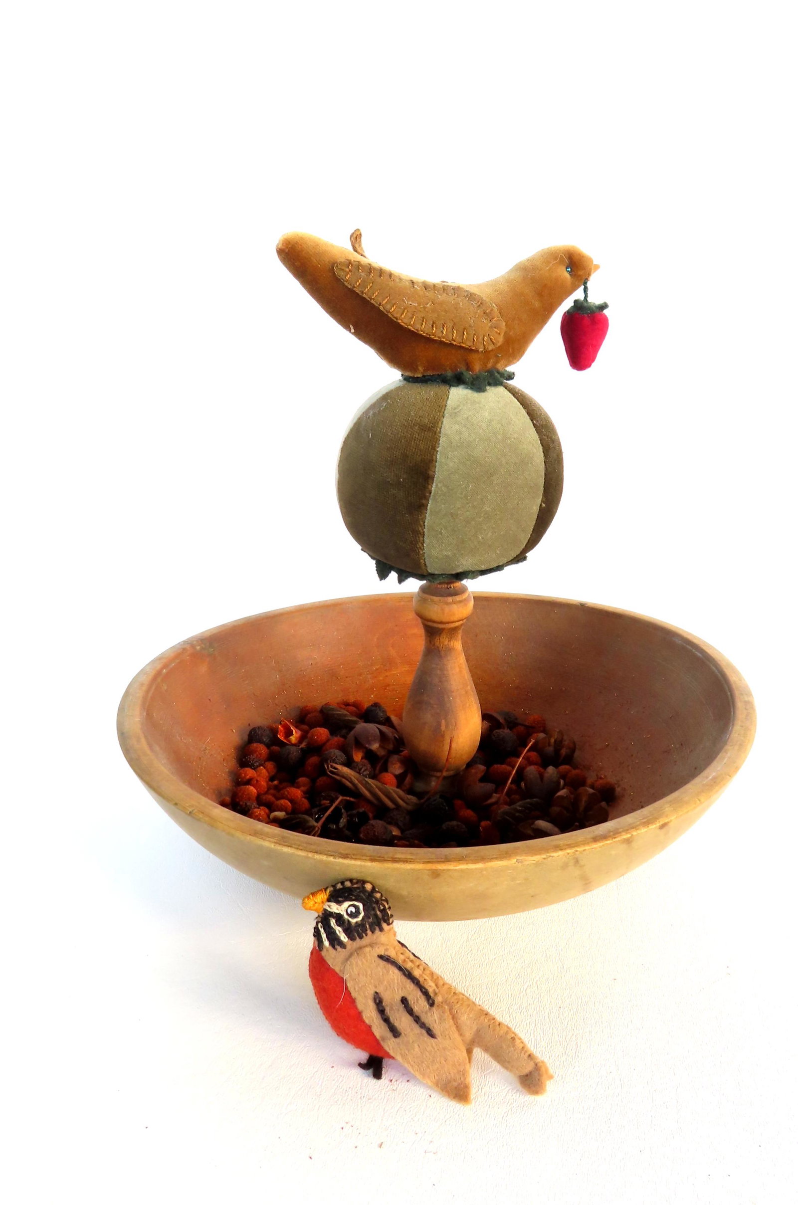 A folk art sewing caddy having a central pin cushion in the form of hand sewn felt bird holding: A folk art sewing caddy having a central pin cushion in the form of hand sewn felt bird holding strawberry in mouth, mounted on circular felt pincushion ball attached to the center of bowl for holding