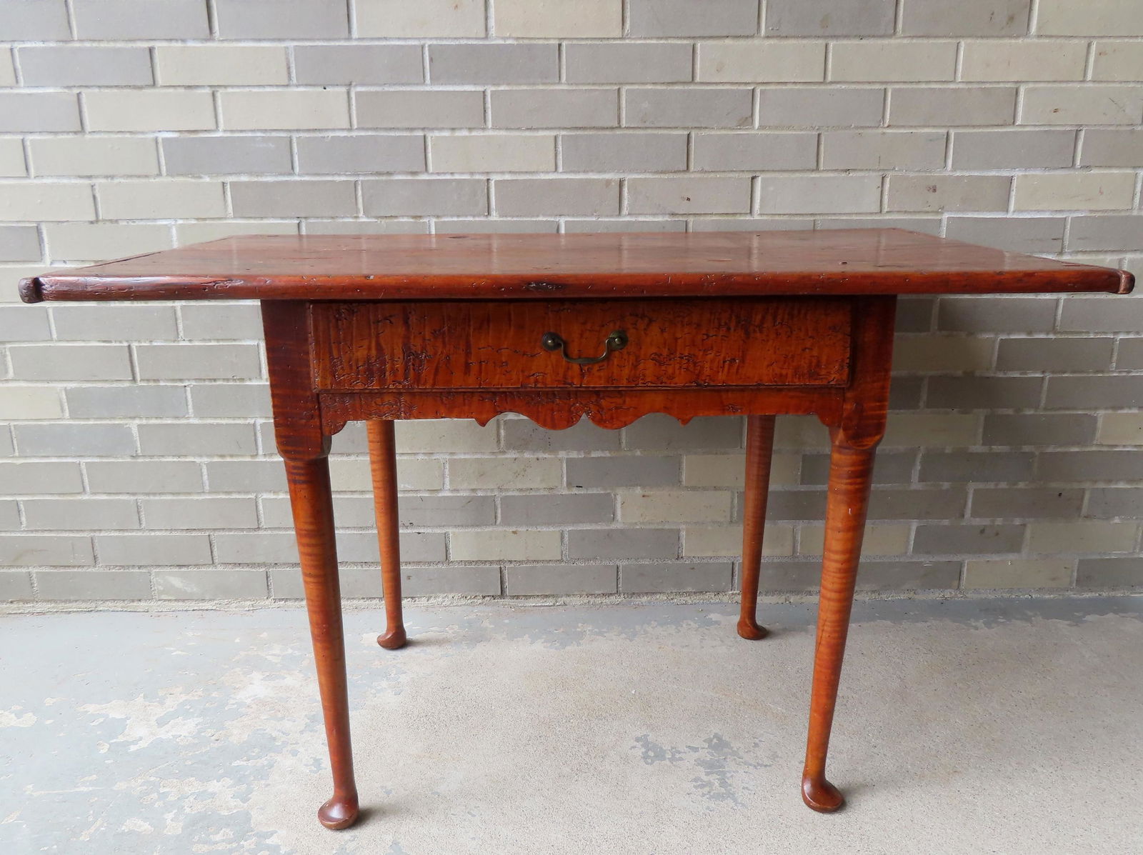 A Queen Ann tiger maple tavern table having a pine one board top with breadboard ends, over 1 long: A Queen Ann tiger maple tavern table having a pine one board top with breadboard ends, over 1 long tiger maple drawer, over a shaped tiger maple apron and turned tiger maple legs leading to pad feet,