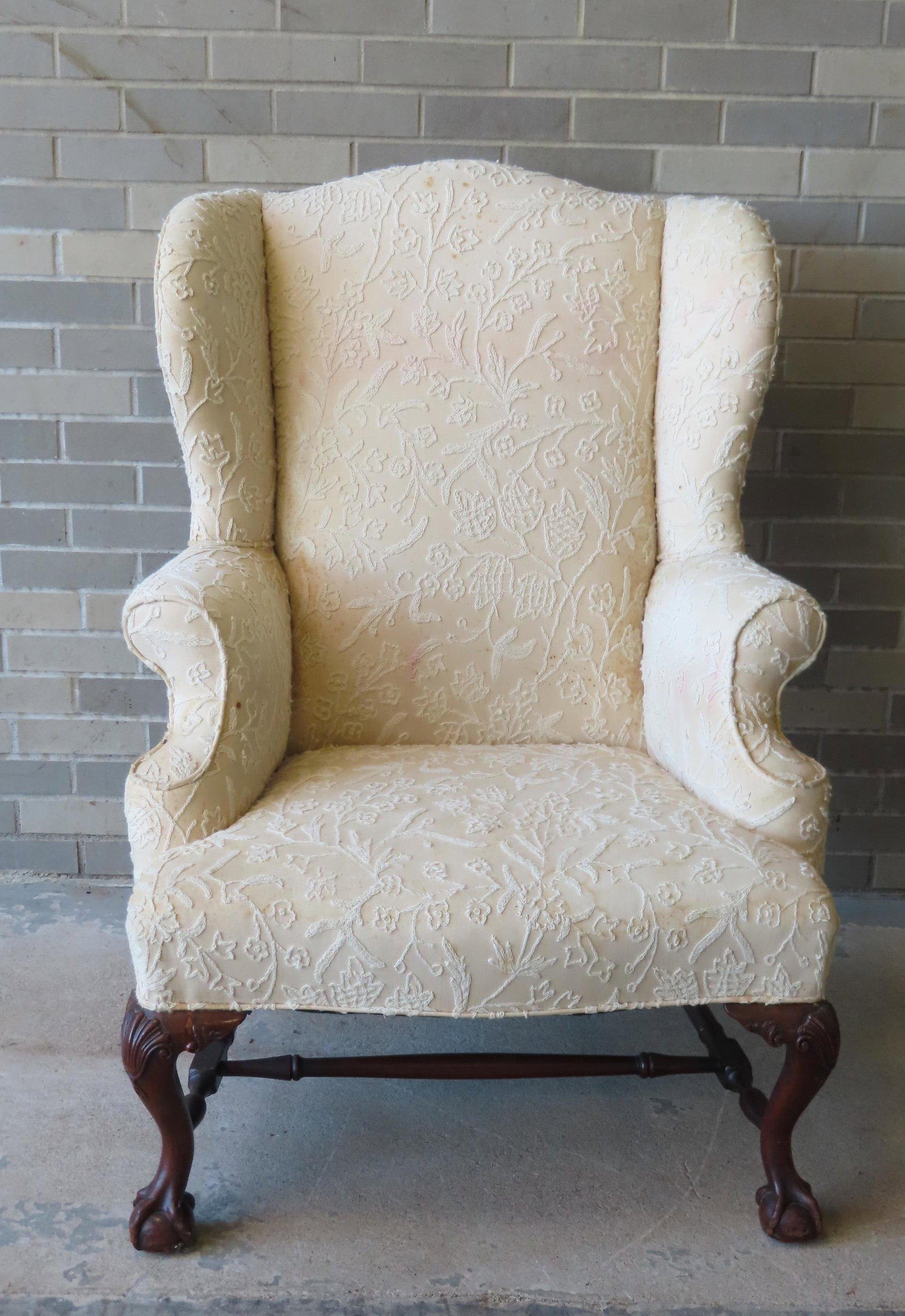A Chippendale style wing chair, with shell carved knees, claw and feet and turned cross stretchers: A Chippendale style wing chair, with shell carved knees, claw and feet and turned cross stretchers and having crewel work upholstery. The upholstery with extensive foxing needs cleaning but it is not 