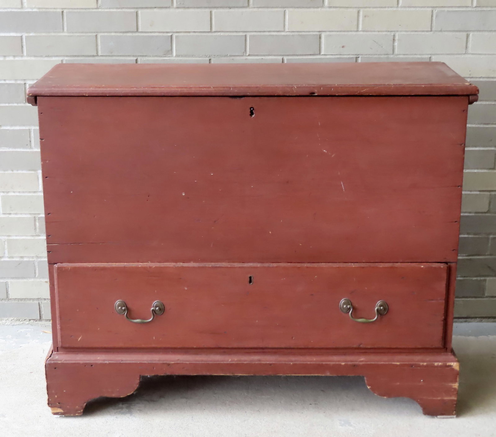 A Queen Ann period blanket box with lower drawer, in original red paint, rattail hinges, molded edge: A Queen Ann period blanket box with lower drawer, in original red paint, rattail hinges, molded edge to lid, original bale pulls and mounted on original bracket base. The base with small repairs, but 
