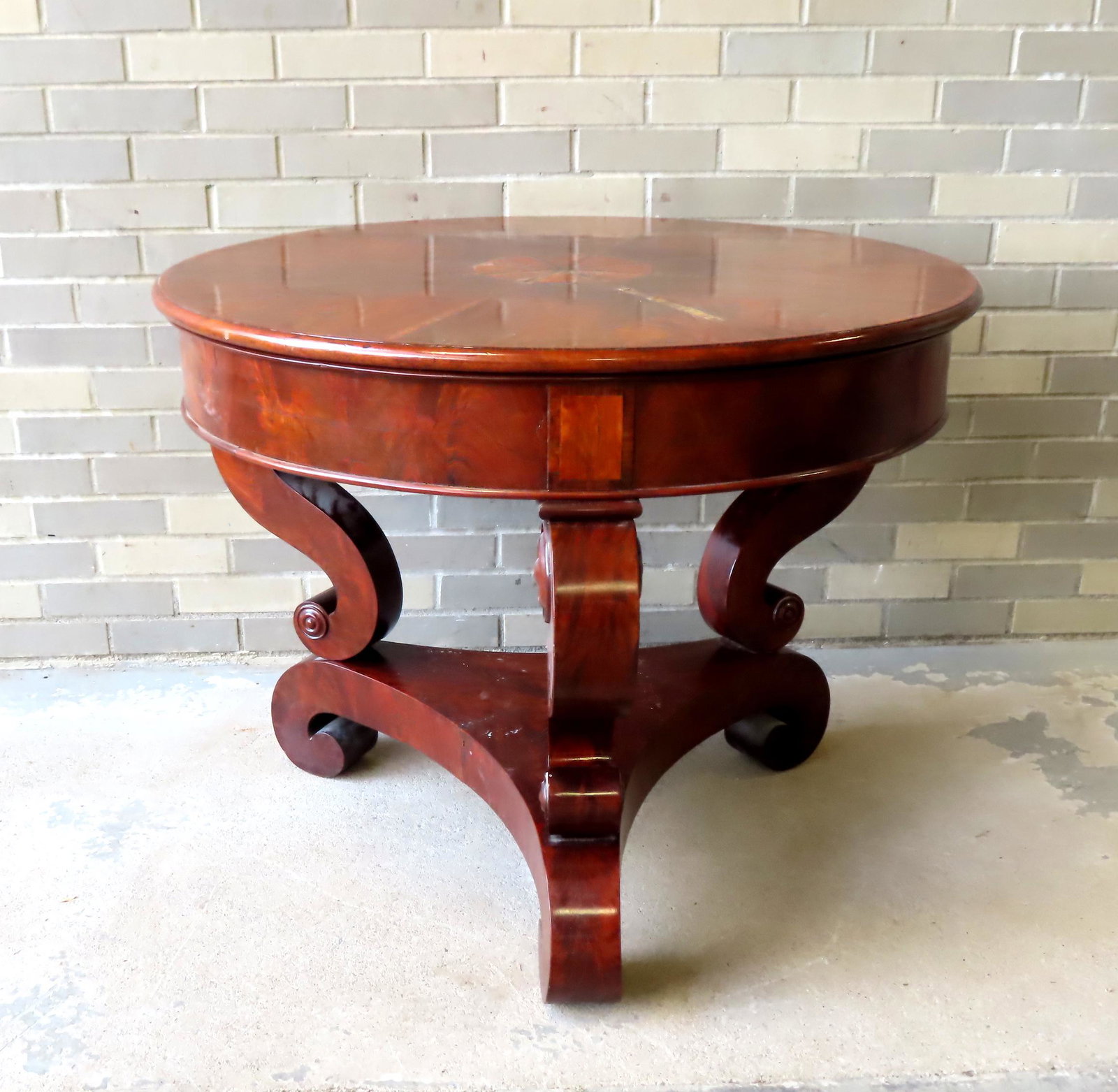 Empire mahogany center table with crotch mahogany top and inlays mounted on scrolled legs leading to: Empire mahogany center table with crotch mahogany top and inlays mounted on scrolled legs leading to lower platform, circa 1850. Some lifting to inlaid panels on top, minor use wear, overall good cond