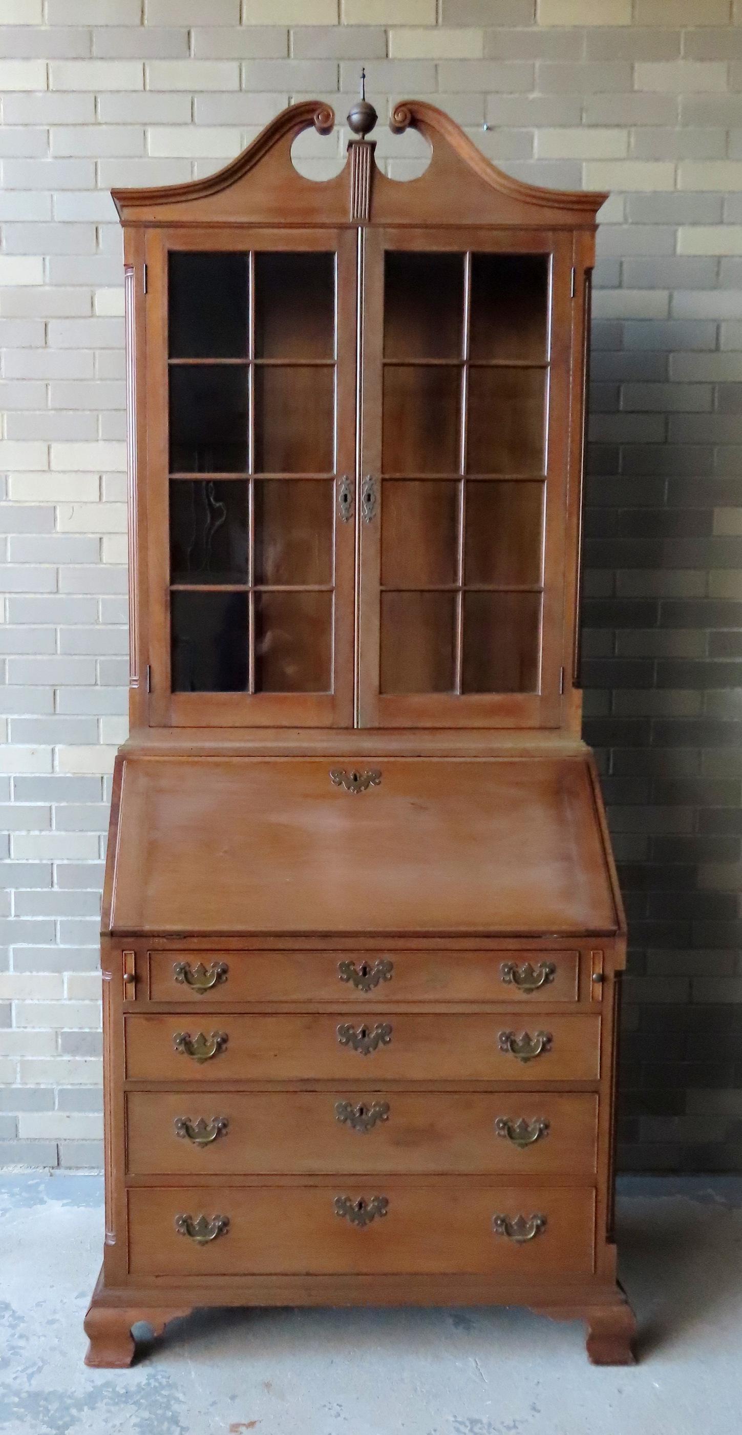 A Chippendale style 2 part secretary cabinet, mid to late 19th century. The top section with broken: A Chippendale style 2 part secretary cabinet, mid to late 19th century. The top section with broken arch top and brass finial, 2 glass doors each with 8 lights with mullions and adjustable shelving on
