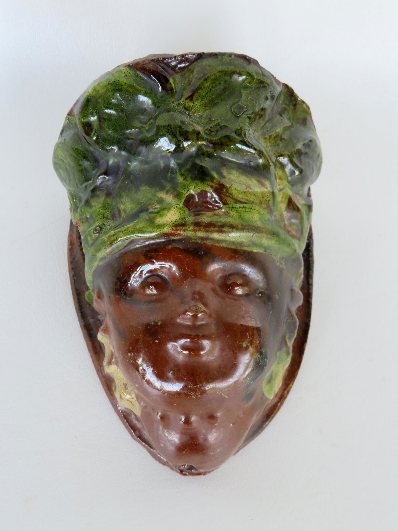 A redware wall pocket that appears to be in the form of a Native American, late 19th century.: A redware wall pocket that appears to be in the form of a Native American, late 19th century. Decorated in slip, with manganese splotches and green paint. Slight roughness on top front edge, else very