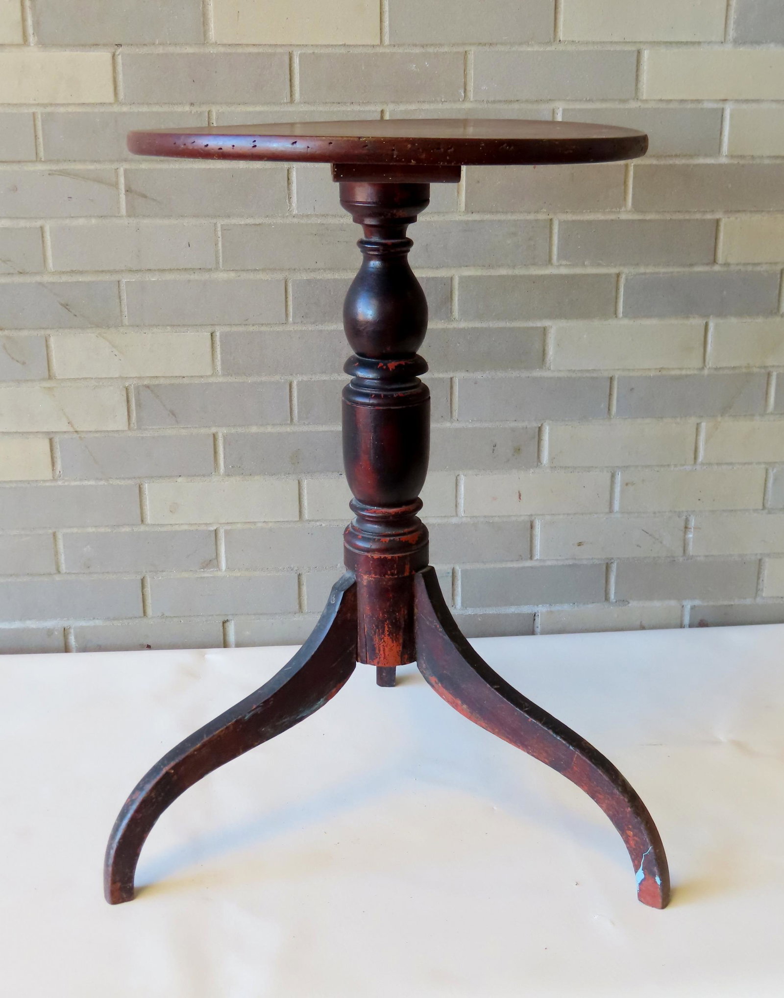 Early candlestand with circular top mounted on turned column, spider legs, circa 1810-20.The top in: Early candlestand with circular top mounted on turned column, spider legs, circa 1810-20.The top in original red stain and the column and legs in original black paint. Small repair to leg where it mee