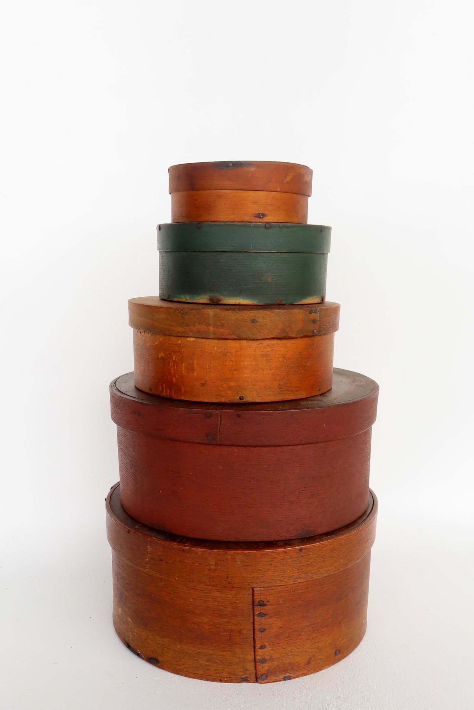 A stack of 5 early pantry boxes in graduated sizes, ranging in size from 4 1/2" diameter x 1 3/4"H: A stack of 5 early pantry boxes in graduated sizes, ranging in size from 4 1/2" diameter x 1 3/4"H to 10 1/4" diameter x 4 3/4"H. Including 1 original green, 1 in original red, and 3 in old natural su