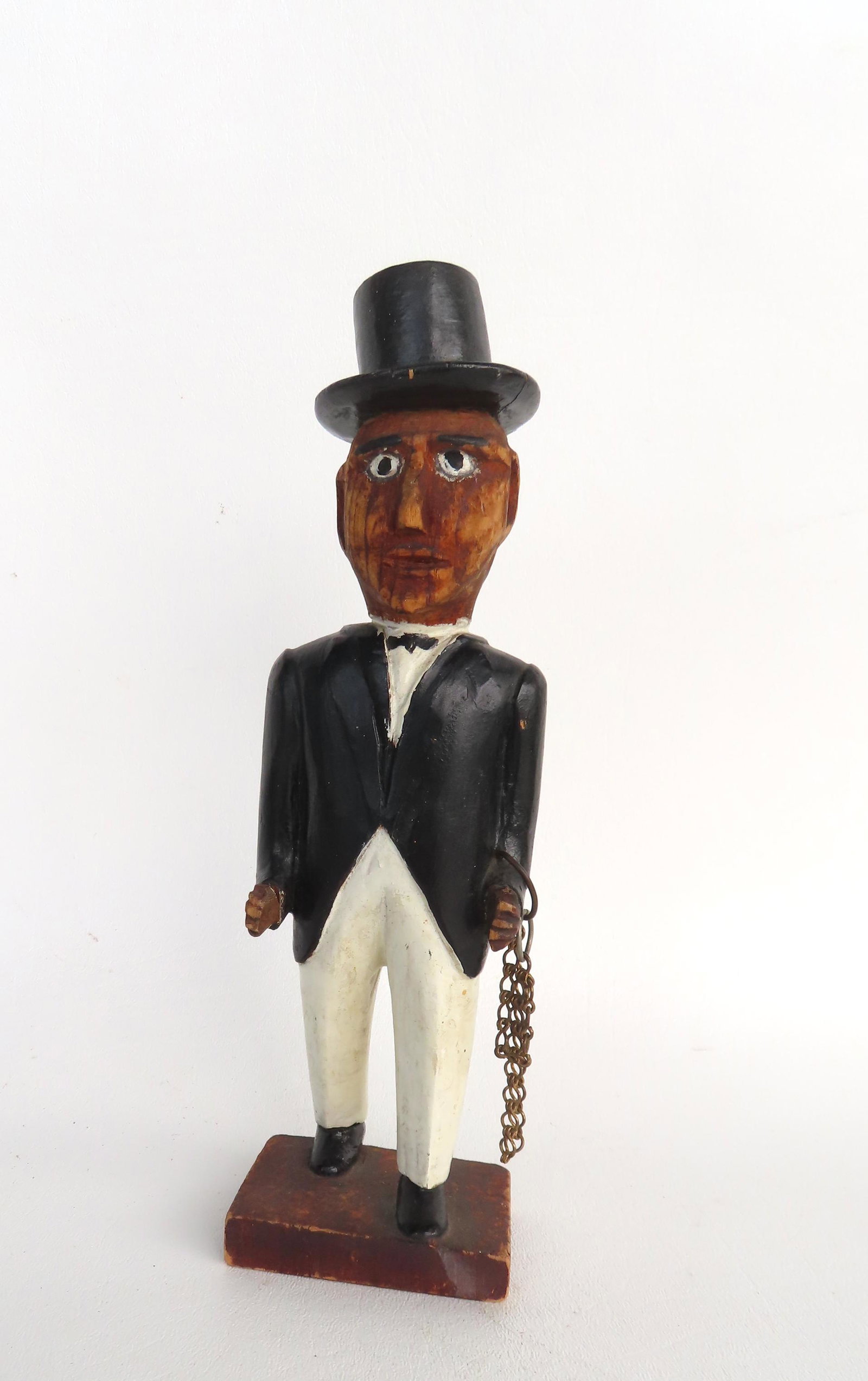 A hand carved folk art figure of a standing man wearing top hat and holding chain, late 19th to: A hand carved folk art figure of a standing man wearing top hat and holding chain, late 19th to early 20th century. The paint is old, but not original. Measures 9 1/4"H x 2 1/2"W.