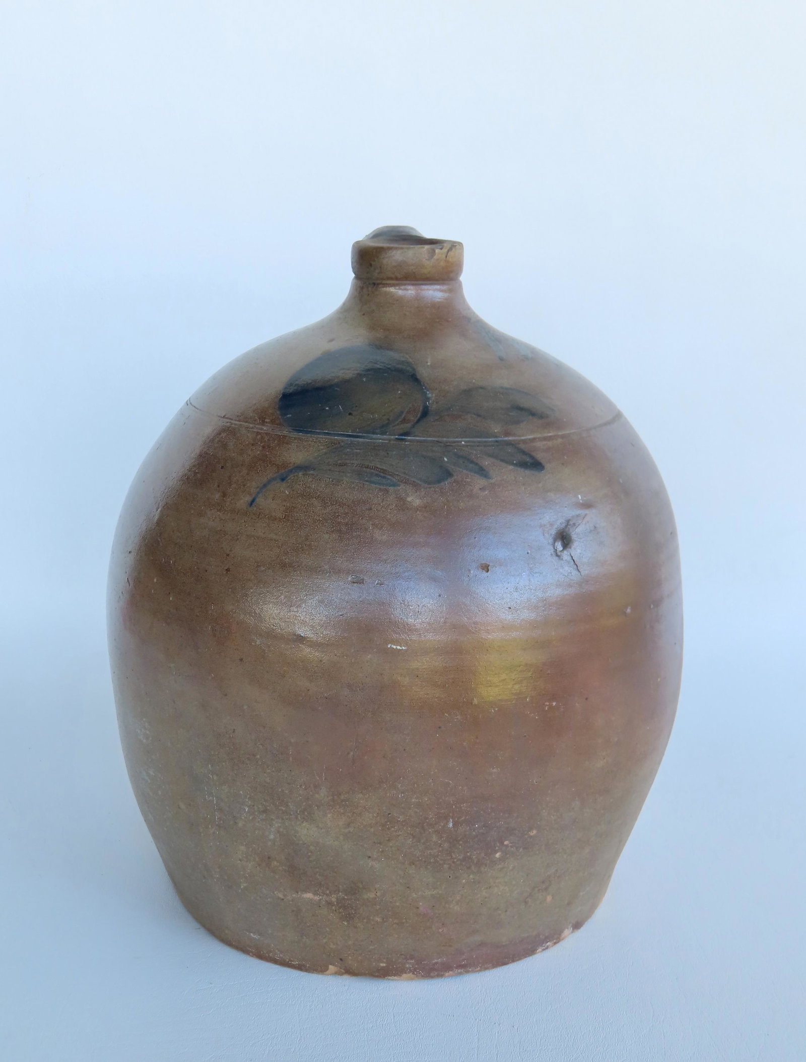 Stoneware jug, decorated with cobalt blue flower, not signed but likely early 19th century with: Stoneware jug, decorated with cobalt blue flower, not signed but likely early 19th century with rounded shape, probably 3 gallon size - measures 13"H x 11"W. Minor chips along bottom edge, else good c