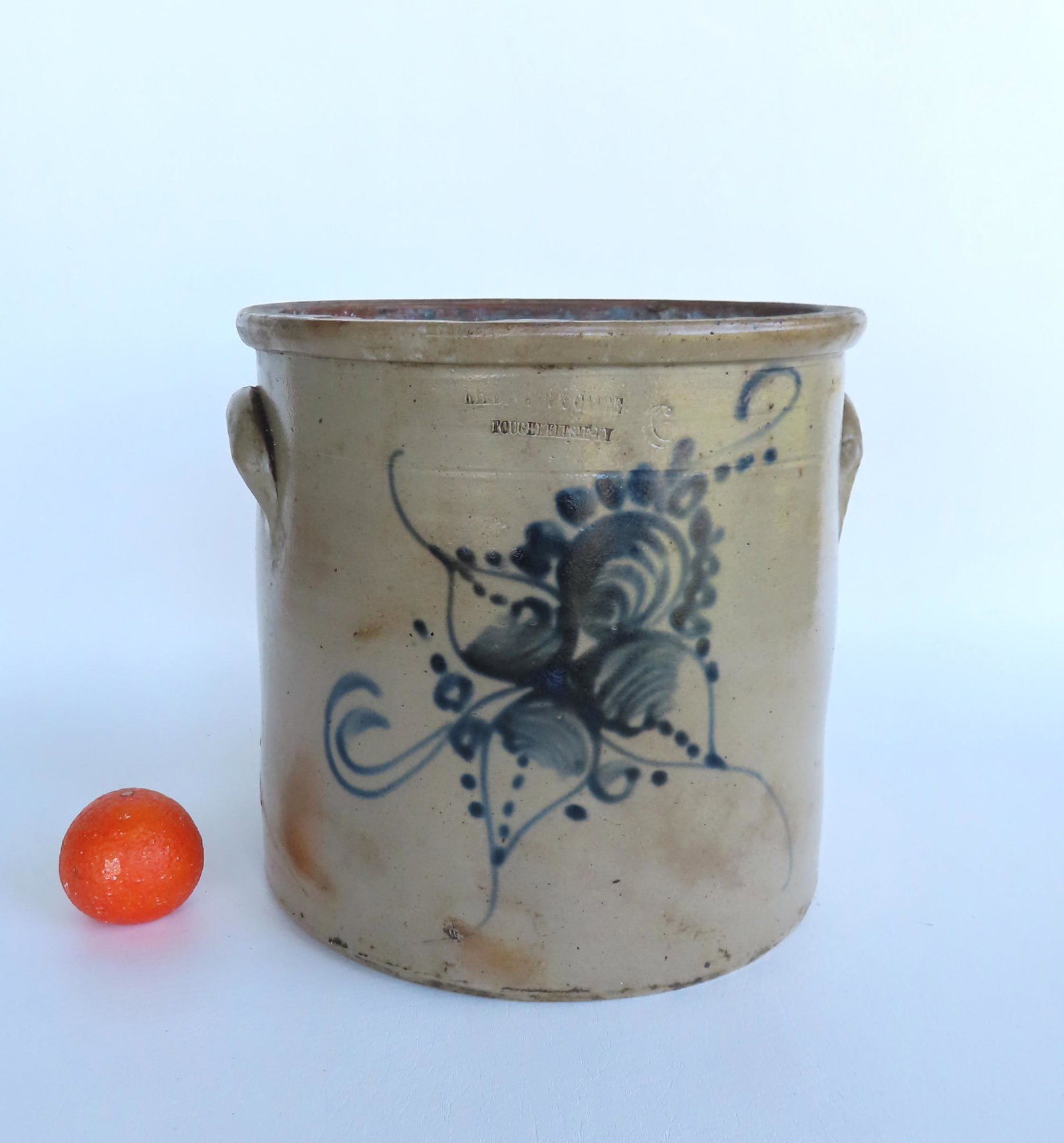 A large stoneware crock decorated with a large cobalt blue flower with the impressed mark of: A large stoneware crock decorated with a large cobalt blue flower with the impressed mark of Riedinger & Caire Poughkeepsie NY, 6 gallon size - small firing burst near base, traces of white substance 