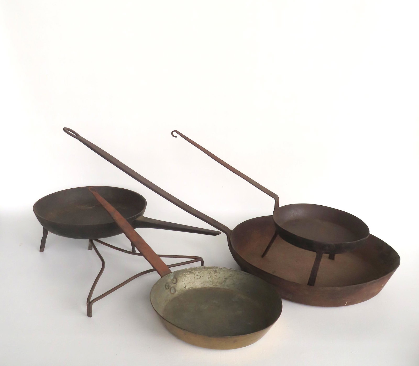 A grouping of 5 early hearth items including a long handle hard forged iron footed frying pan, a: A grouping of 5 early hearth items including a long handle hard forged iron footed frying pan, a cast iron footed long handled frying pan, a brass frying pan with iron handle, a small iron trivet, and