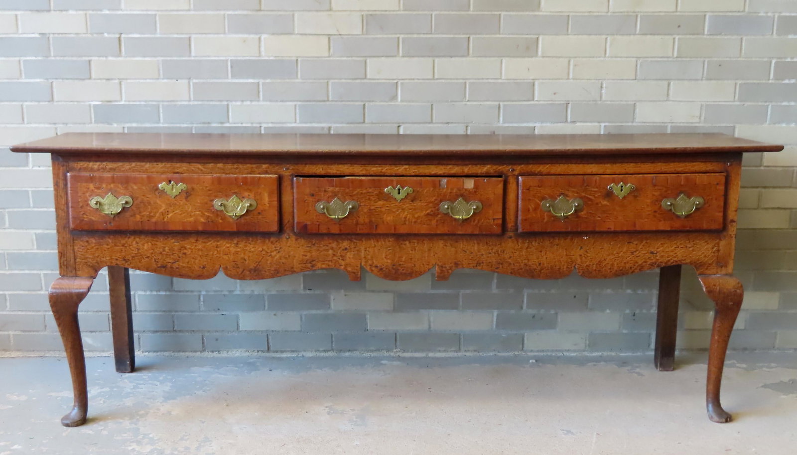 A Queen Ann oak Welsh cupboard base having 3 drawers banded with mahogany.: A Queen Ann oak Welsh cupboard base having 3 drawers banded with mahogany, matching engraved batwing pulls and escutcheons (old, but probably not original), and having front cabriole legs leading to p