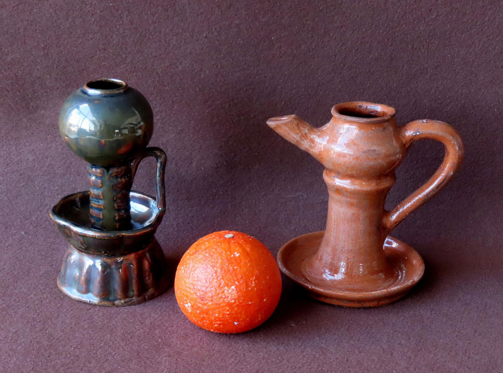 Two earthenware fat burning lamps. The first in a red- orange glaze that appears to be redware,: Two earthenware fat burning lamps. The first in a red- orange glaze that appears to be redware, probably Pennsylvania - 5 3/4"W x 6"H - very good condition; the second with a Rockingham-like glaze, un