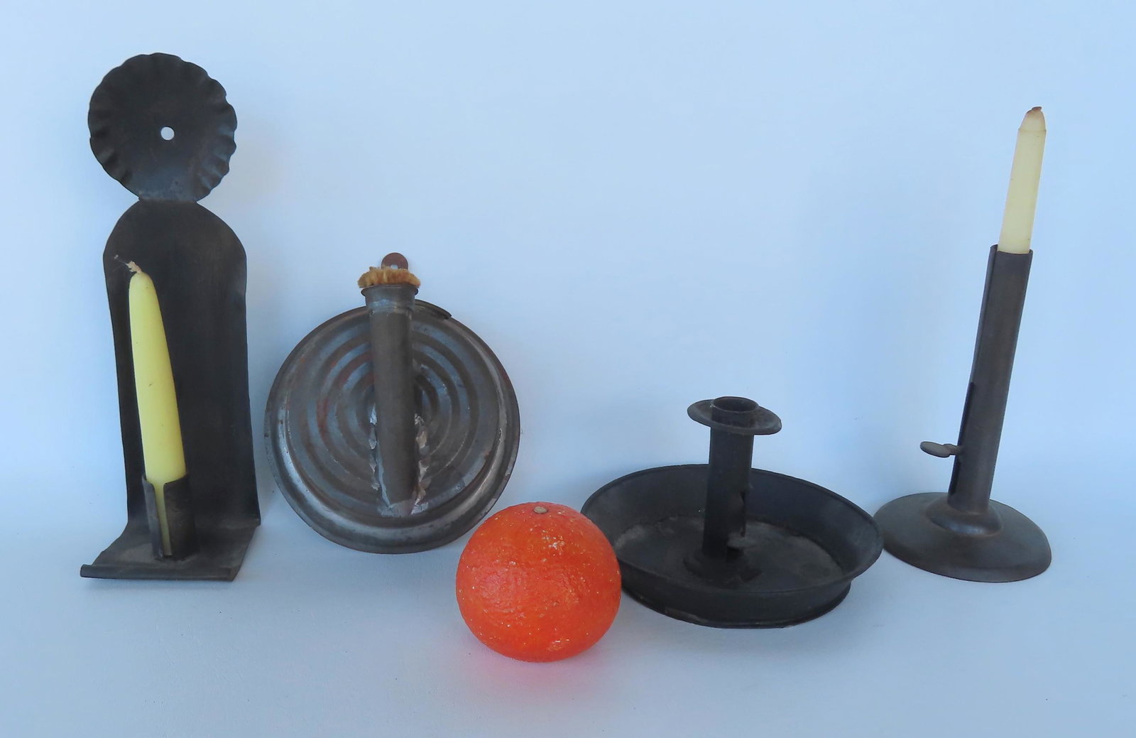 Grouping of 4 early tin lighting devices including hog scraper candlestick, pushup chamberstick with: Grouping of 4 early tin lighting devices including hog scraper candlestick, pushup chamberstick with candle drip pan, a candle wall sconce with crimped top, and a fat burning wall hanging lamp. The la