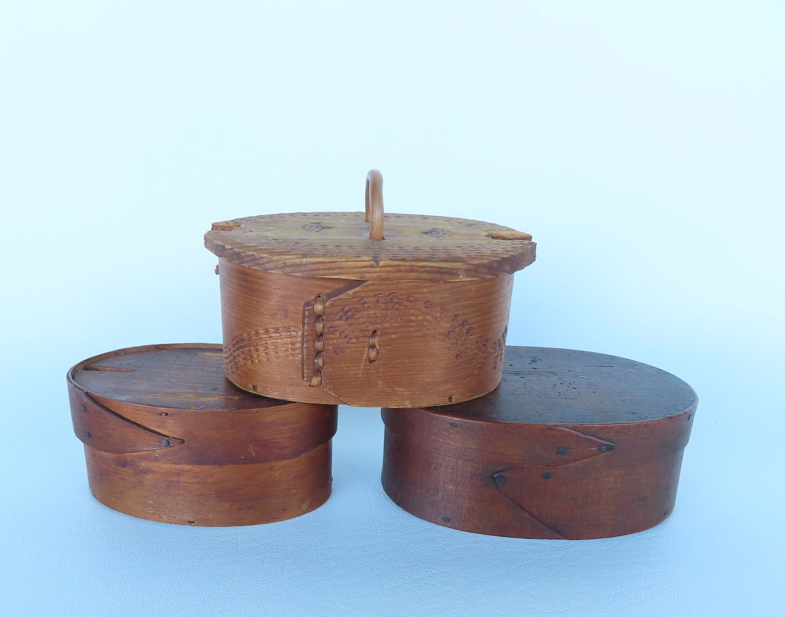 Three small oval boxes. Two American in darkened original finish with single finger - the largest 5: Three small oval boxes. Two American in darkened original finish with single finger - the largest 5 1/4"W x 2"H - both in good condition; and 1 Norwegian with etched design with wooden key - locking m