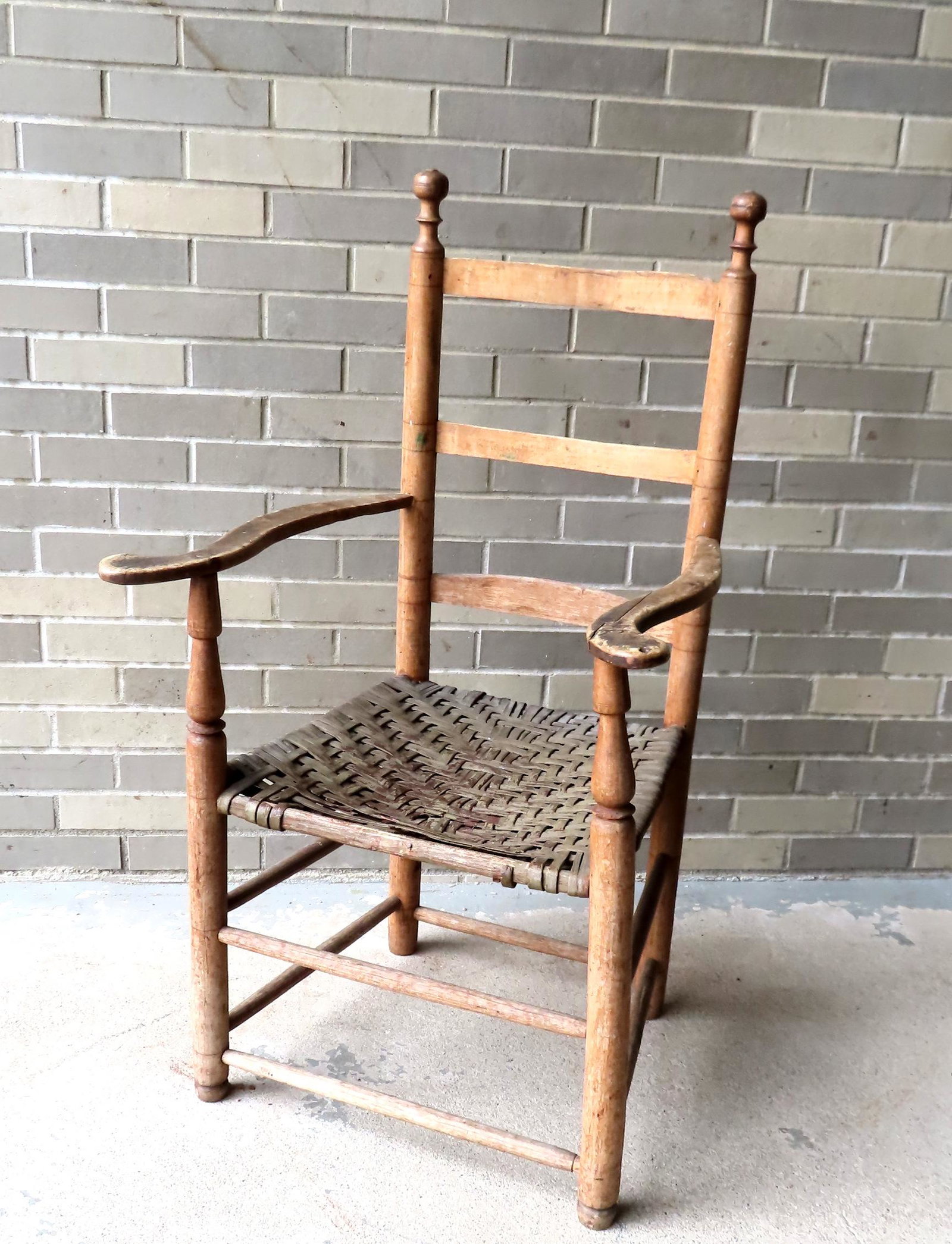 A Hudson Valley ladder back chair with scrolled arms retaining original woven cane seat, 18th: A Hudson Valley ladder back chair with scrolled arms retaining original woven cane seat, 18th century. The arms with wear and one with hairline and carved initial, original worn cross stretchers, loss