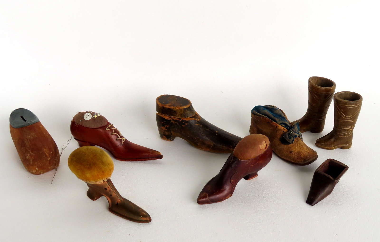Grouping of 9 miniature shoes and boot whimsies, most hand carved wood 19th century. Notables: Grouping of 9 miniature shoes and boot whimsies, most hand carved wood 19th century. Notables include inkwell (missing resevoir insert), pincushions (one converted from a real child's shoe inscribed o