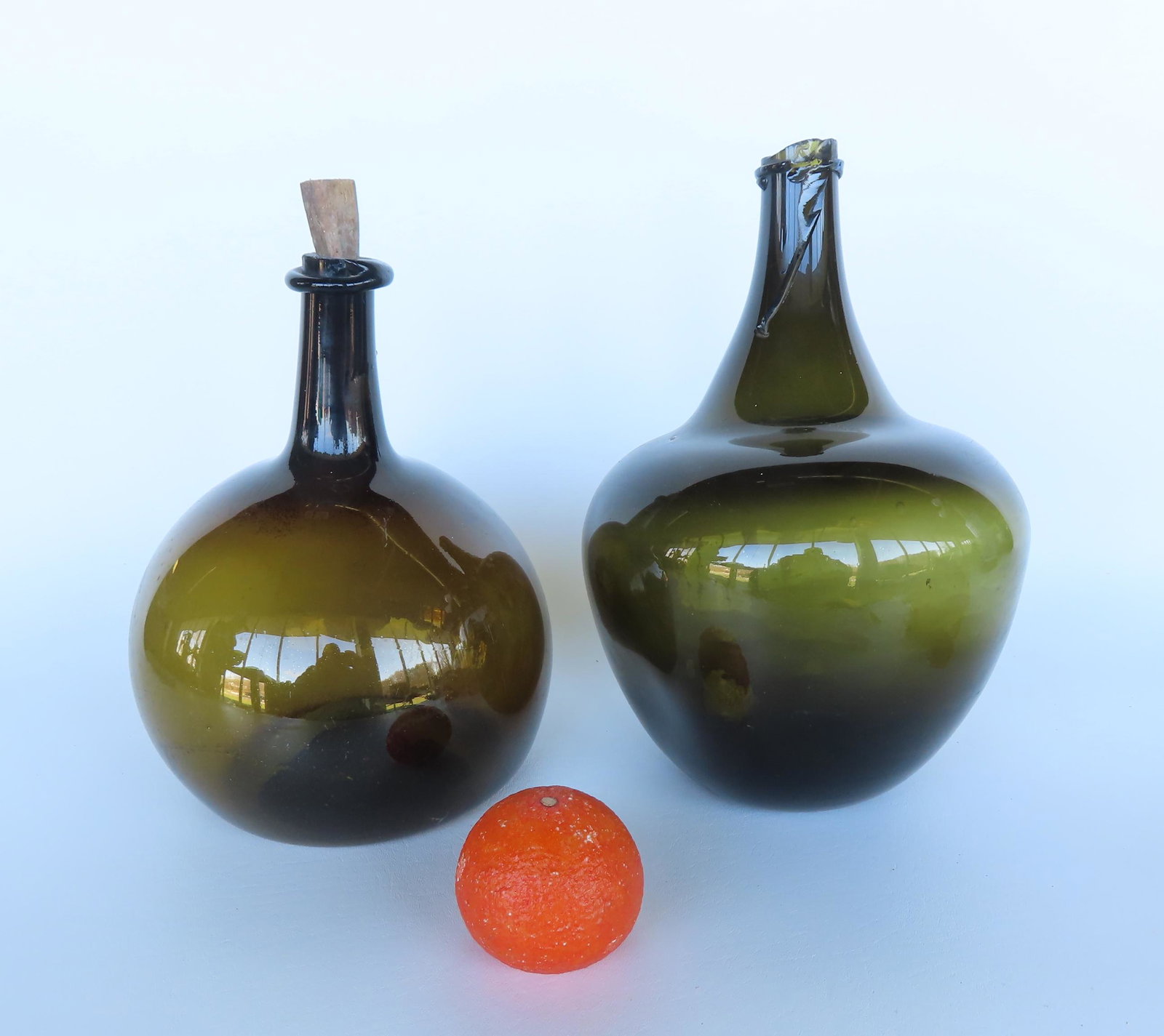 Two olive green demijohn bottles with crudely sheared mouths with string rims, both probably 18th: Two olive green demijohn bottles with crudely sheared mouths with string rims, both probably 18th century - the bulbous with kicked up bottom and scarred pontil and is in very good condition - 10 1/4"