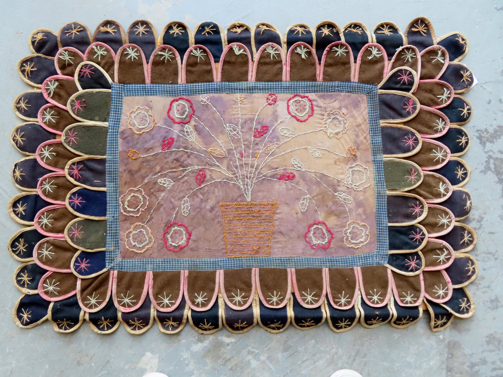 A folk art table rug having an embroidered central image of flowers in a pot, and the bordering tabs (1 of 6)