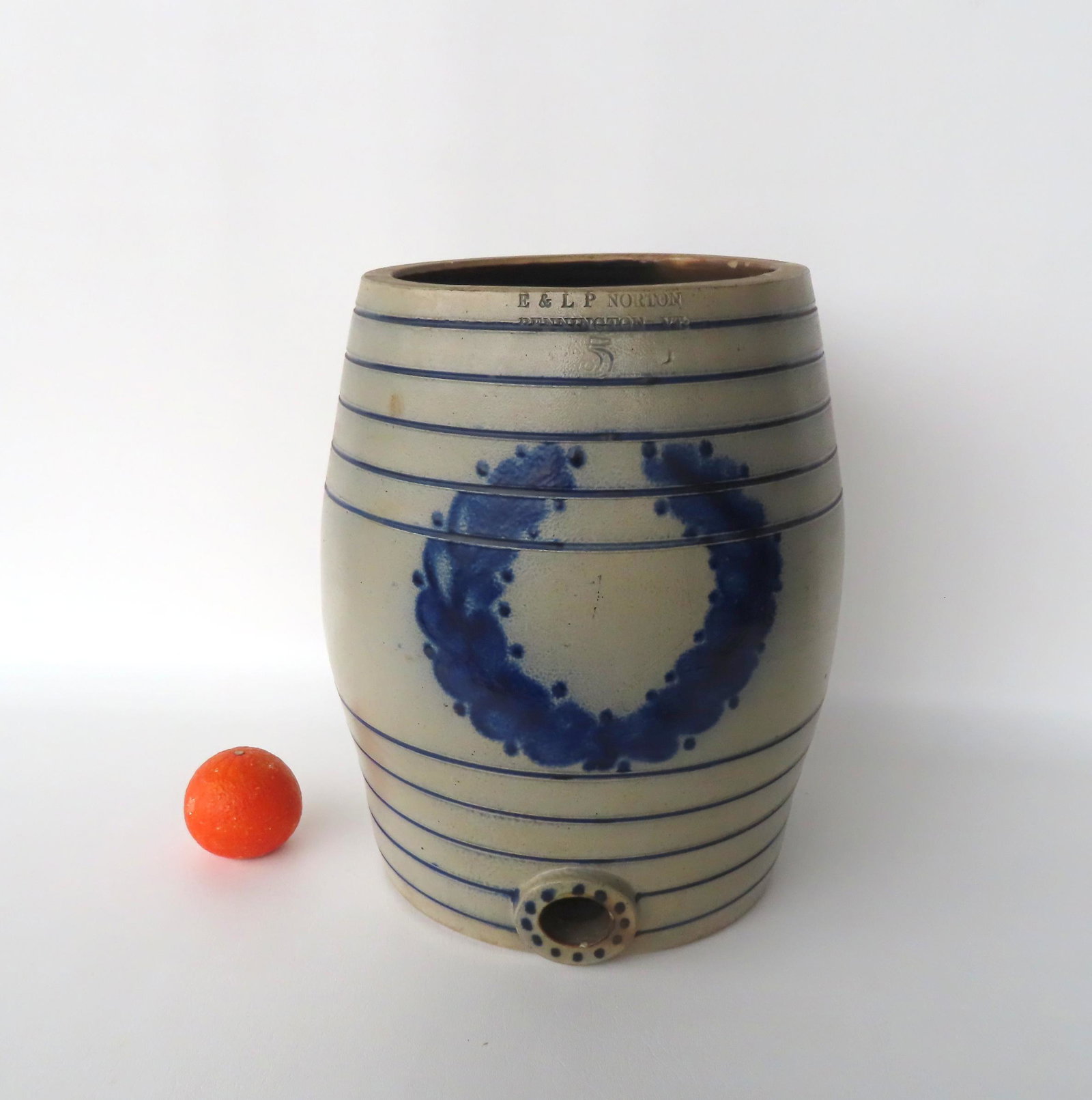A stoneware 5 gallon water cooler with the impressed mark of "E & L.P. Norton / Bennington VT" -: A stoneware 5 gallon water cooler with the impressed mark of "E & L.P. Norton / Bennington VT" - decorated with a cobalt blue wreath about spout decorated with blue dots. Several tiny rim chips and a 