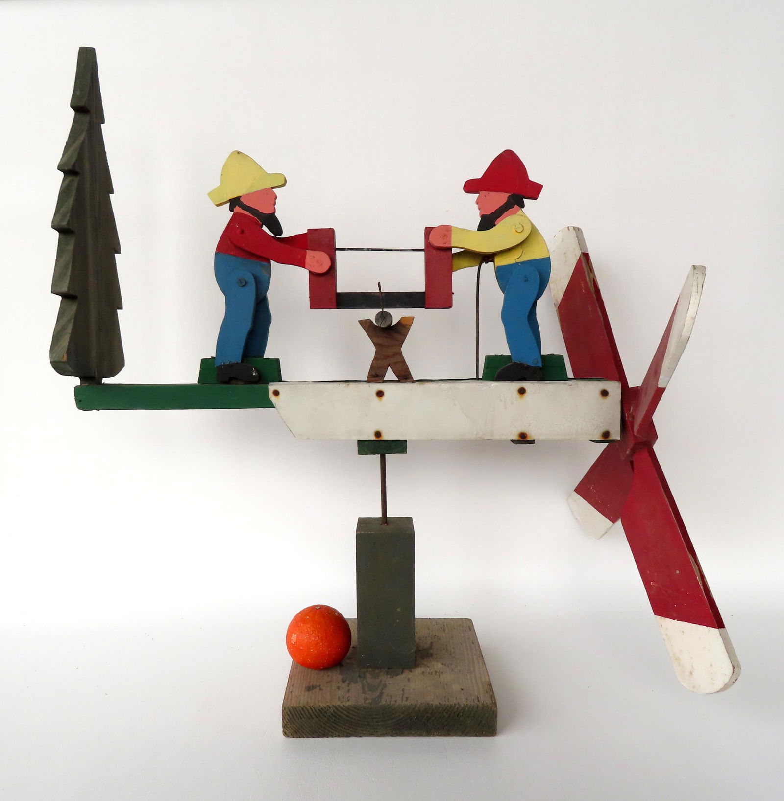 A wooden hand painted whirligig depicting 2 men cutting a log adjacent to evergreen tree. Very good (1 of 7)