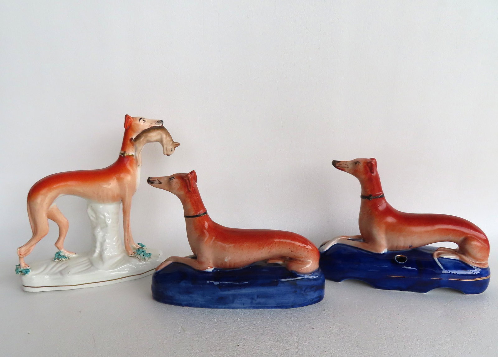 Three greyhound Staffordshire figures, all hand painted, including one with rabbit in mouth - small: Three greyhound Staffordshire figures, all hand painted, including one with rabbit in mouth - small loss to flowers at bottom of right front foot, else very good condition - 7"W x 7 1.2"H, and 2 recli