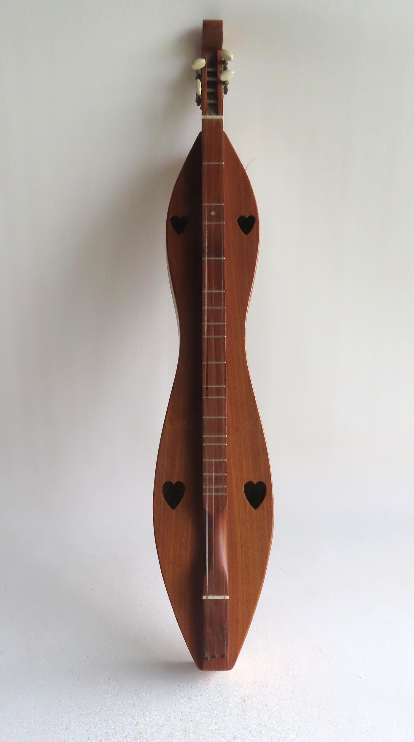 A walnut dulcimer with 4 heart cutouts and 4 strings, signed "Handcrafted By Folkcraft Instruments / (1 of 9)