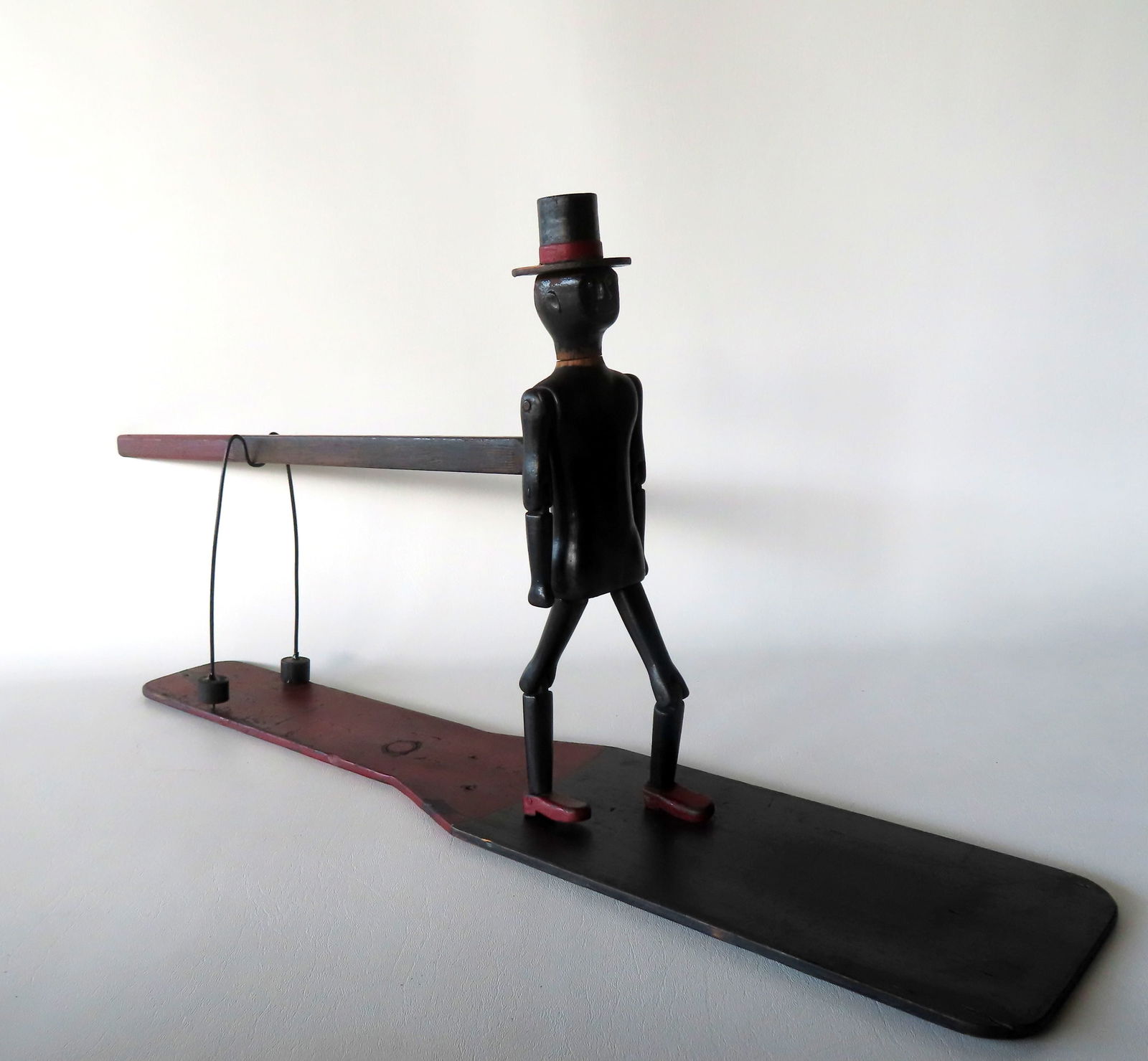 A folk art African American jigger toy depicting a dancing man with hat and glass eyes,  red and (1 of 13)