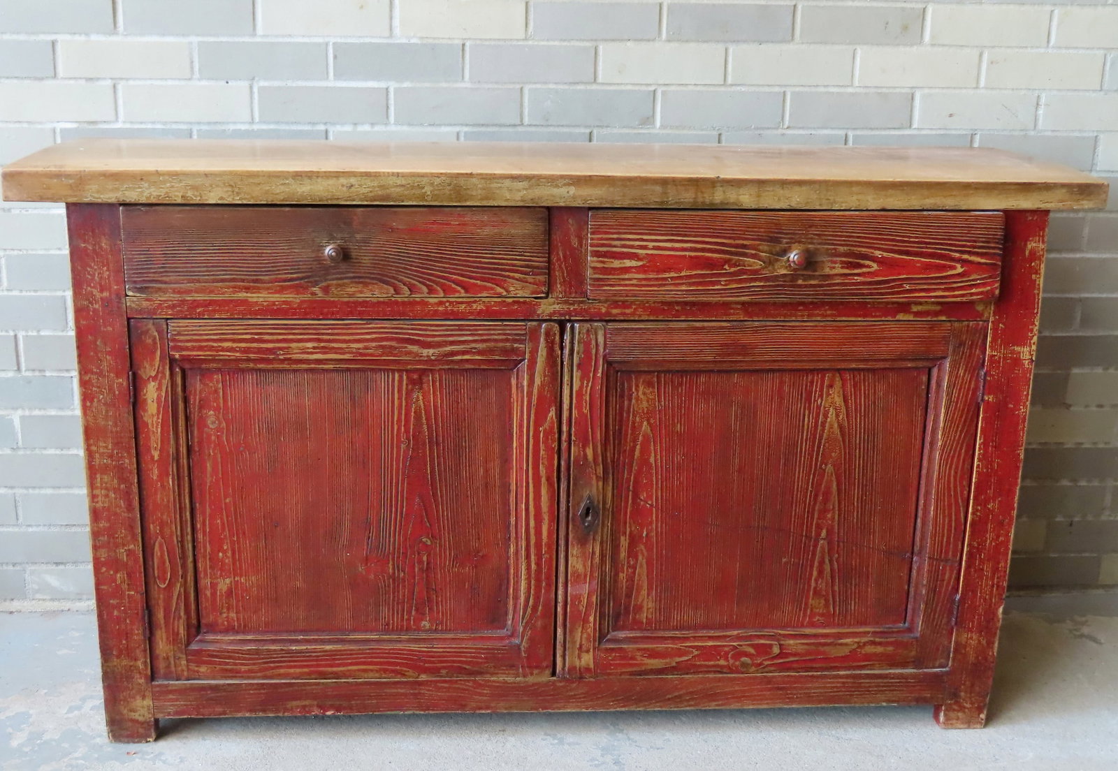 A small sideboard in old red paint and scrubbed top having 2 dovetailed drawers over 2 doors with: A small sideboard in old red paint and scrubbed top having 2 dovetailed drawers over 2 doors with lock and key. The back edge of the top with a chunk of wood missing only noticeable on reverse side, e